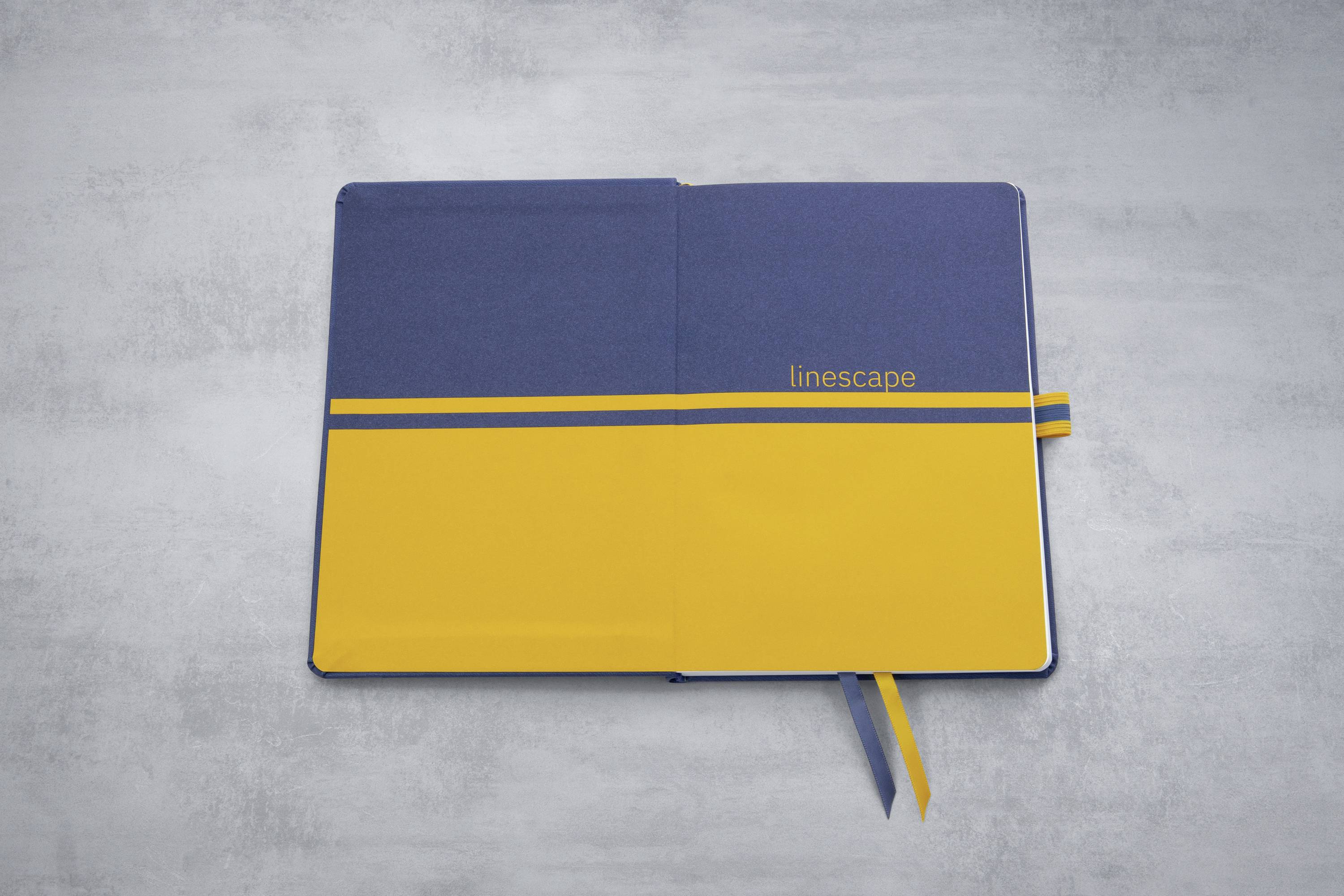 Aufgeschlagenes Notizbuch mit blauem und gelbem Einband. Der Text 'linescape' ist auf der rechten Seite sichtbar.