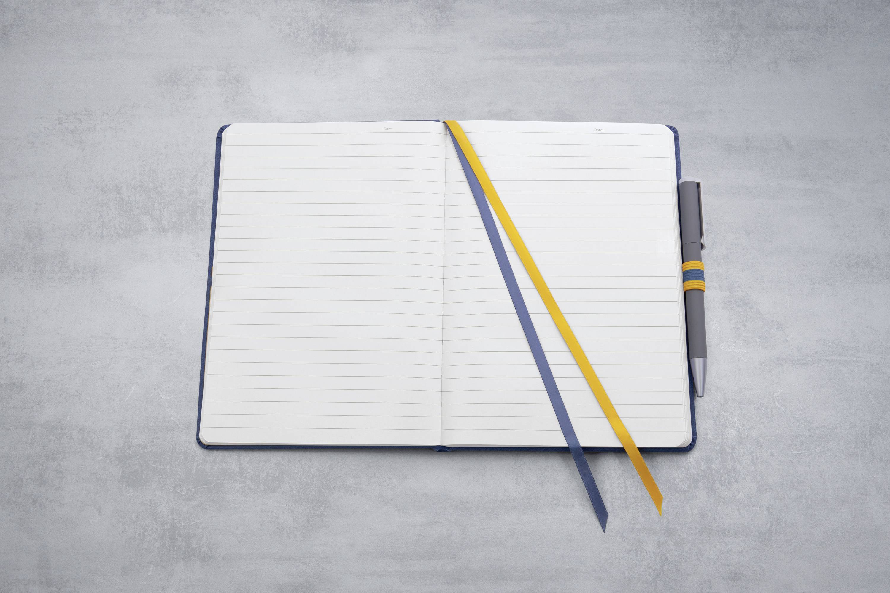 Ein offenes Notizbuch mit weißen, linierten Seiten. Zwei farbige Lesezeichen und ein Kugelschreiber liegen diagonal auf den Seiten.