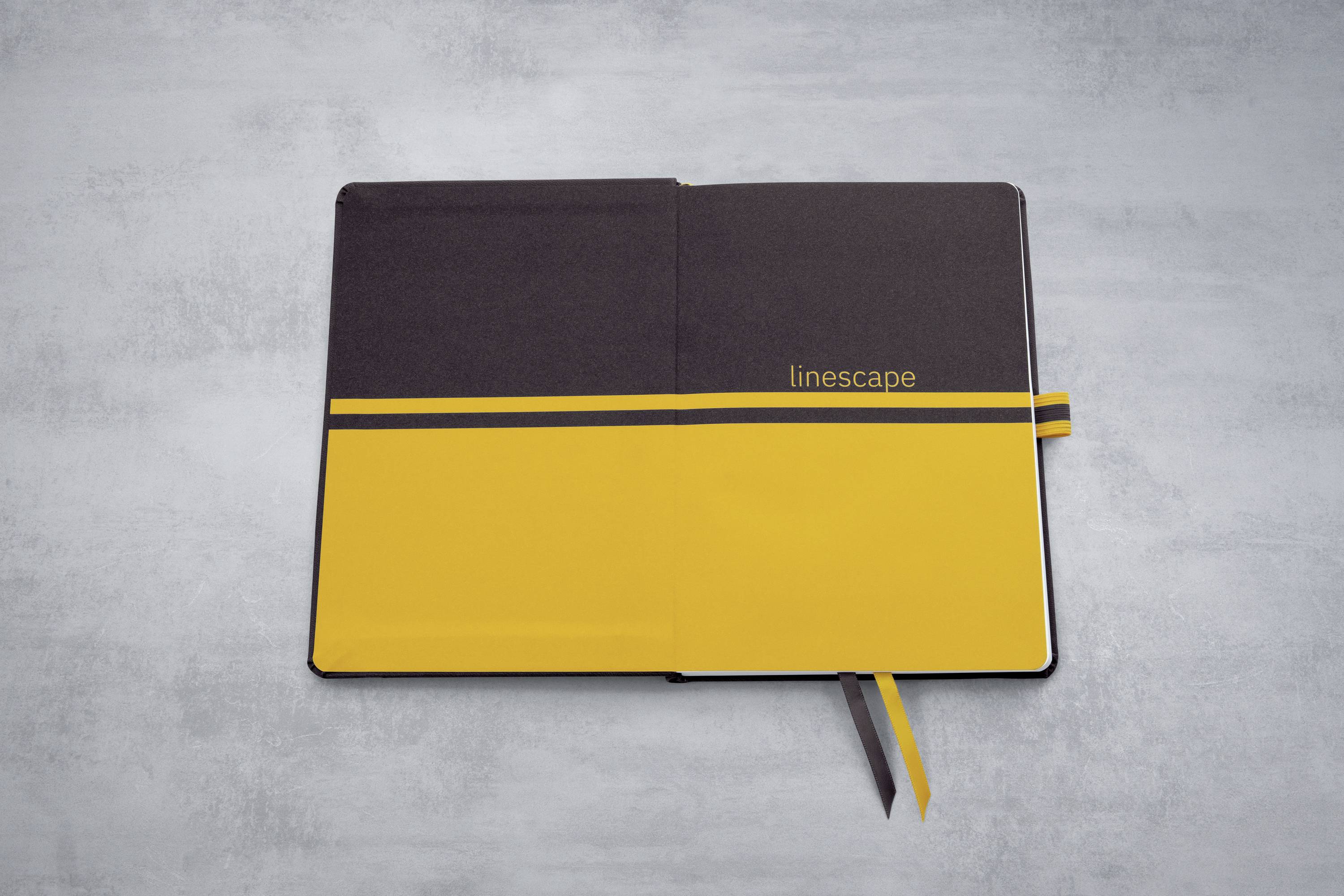 Ein Notizbuch mit schwarzem und gelbem Einband, geöffnet auf einer grauen Oberfläche. Rechts steht in kleiner Schrift 'linescape'.