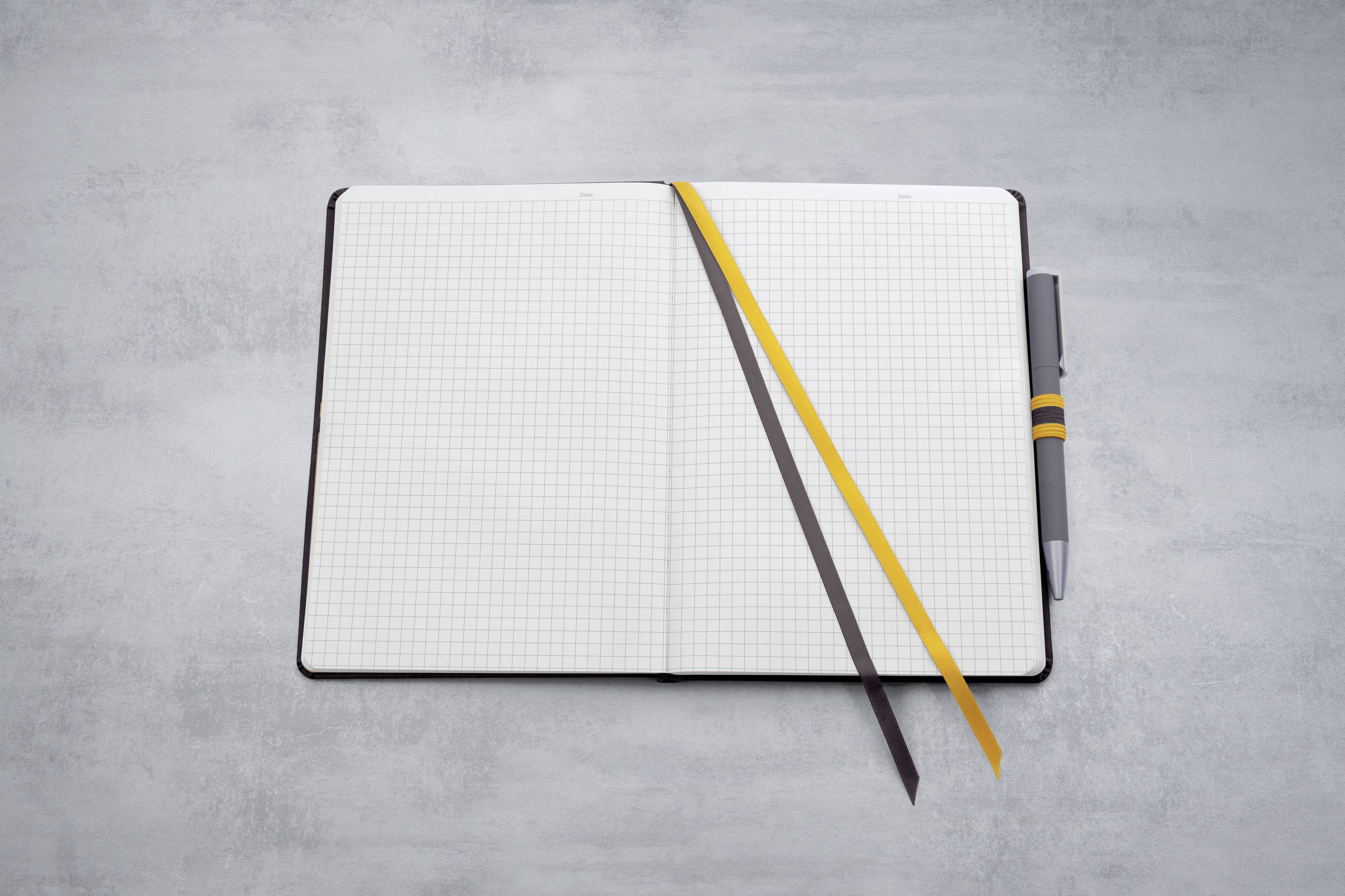 Ein offenes Notizbuch auf einem Tisch, mit karierten Seiten, zwei Lesezeichenbändern und einem Stift an der rechten Seite.