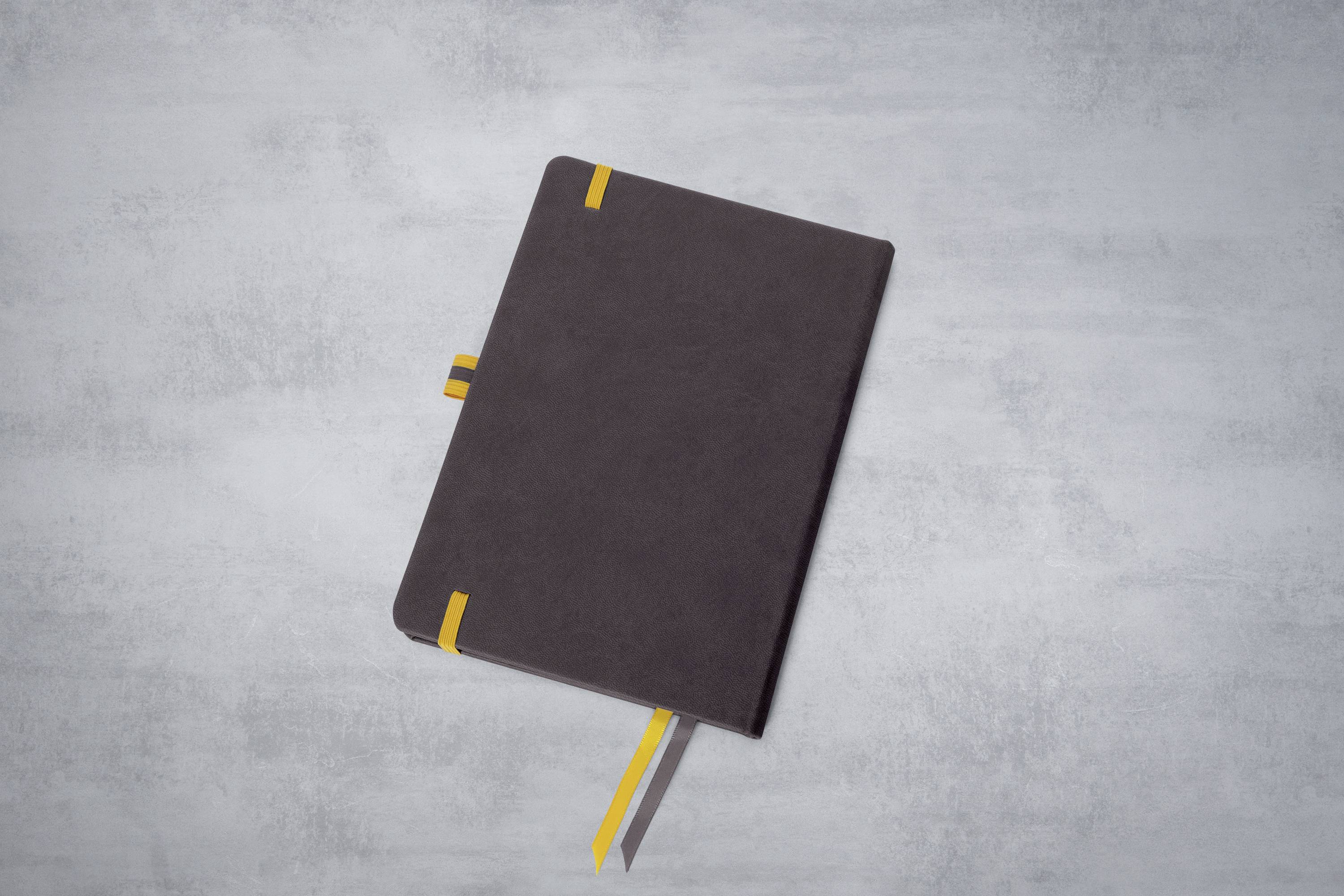 Dunkles Notizbuch mit gelben Markierungsstreifen liegt auf einem grauen Hintergrund.