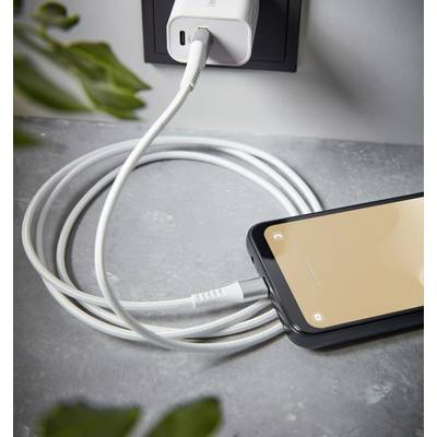 Ein Smartphone wird mit einem weißen Kabel an einer Steckdose geladen. Das Handy liegt auf einem Tisch, das Kabel ist aufgerollt.