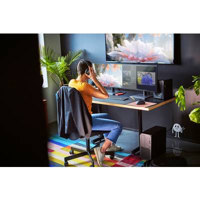 Eine Person sitzt an einem Schreibtisch mit drei Bildschirmen, trägt Kopfhörer und arbeitet in einem modern eingerichteten Büro.