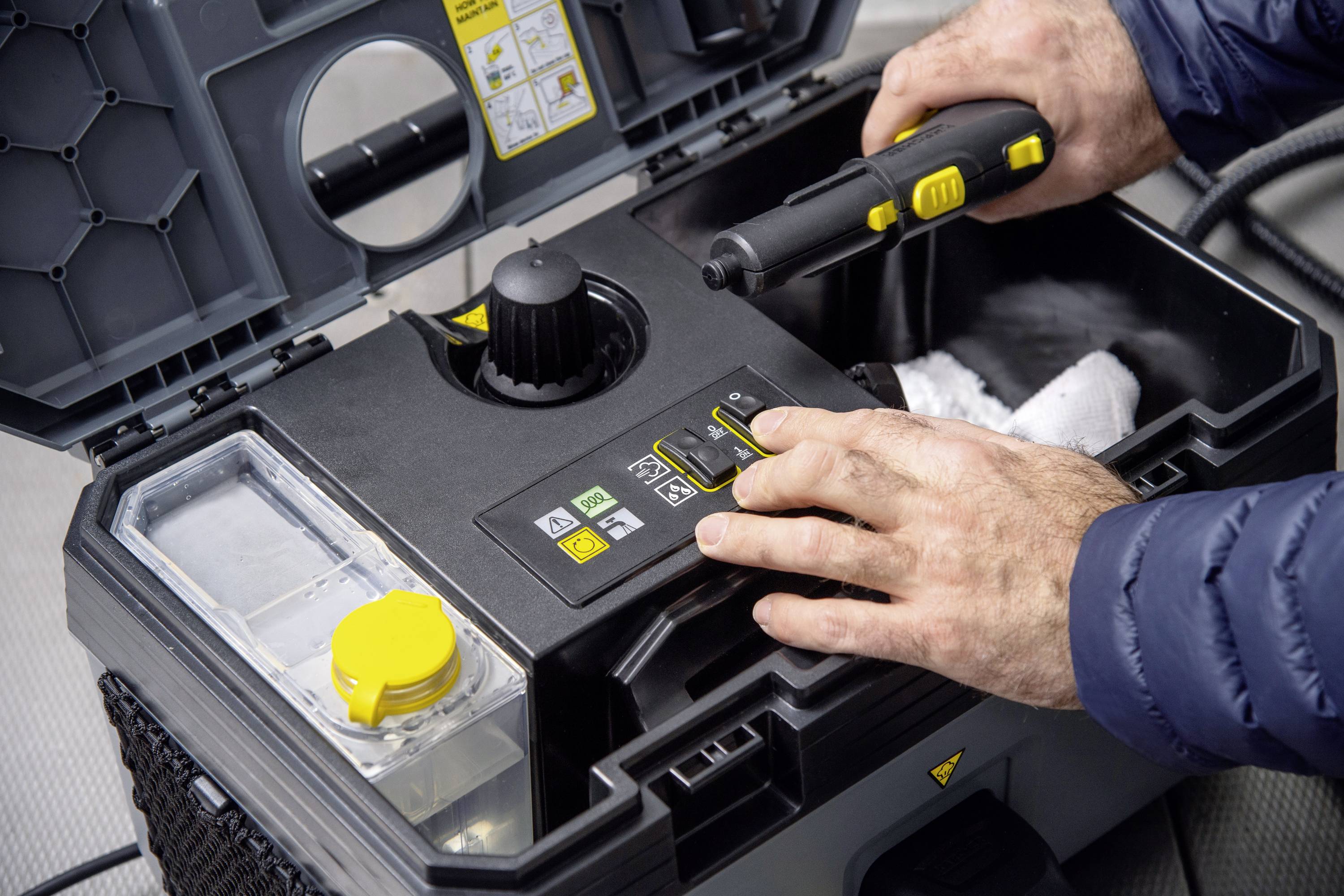 Person bedient eine Reinigungsmaschine mit mehreren Tasten und einem abnehmbaren Tank. Hände und Steuerungselemente sind im Fokus.