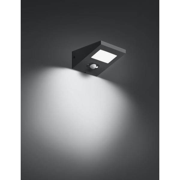 Schwarze Wandleuchte mit quadratischem Lampenschirm, strahlt weiches Weißlicht aus, beleuchtet Wand von oben.
