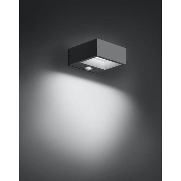 Eine quadratische Wandleuchte strahlt ein weiches Licht nach unten aus, beleuchtet die Wand und den Raum darunter in einem dunklen Raum.
