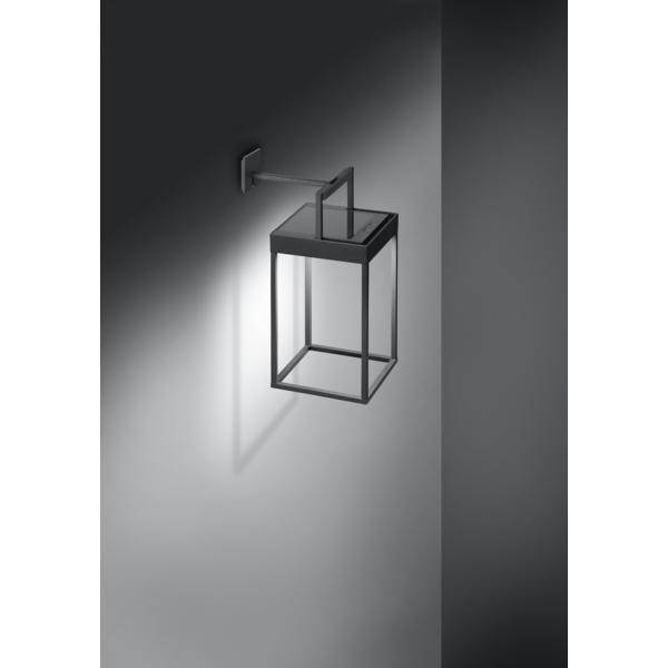 Wandmontierte, moderne Außenlampe aus Metall mit quadratischem Schirm, die weiches Licht auf eine graue Wand wirft.