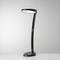 Eine schwarze, moderne Schreibtischlampe mit gebogenem Arm steht auf einem grauen Hintergrund.