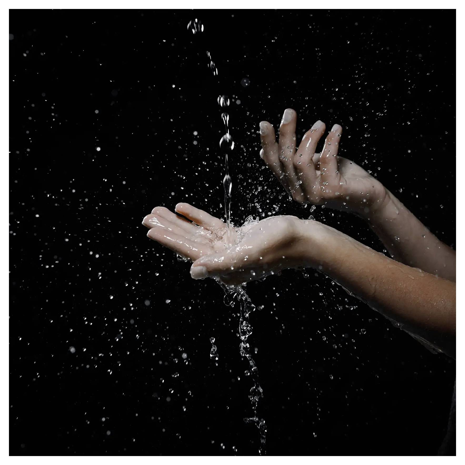 Hände, die einen Wasserstrahl vor schwarzem Hintergrund auffangen, wobei der Fluss und die Spritzer von Wassertropfen betont werden.