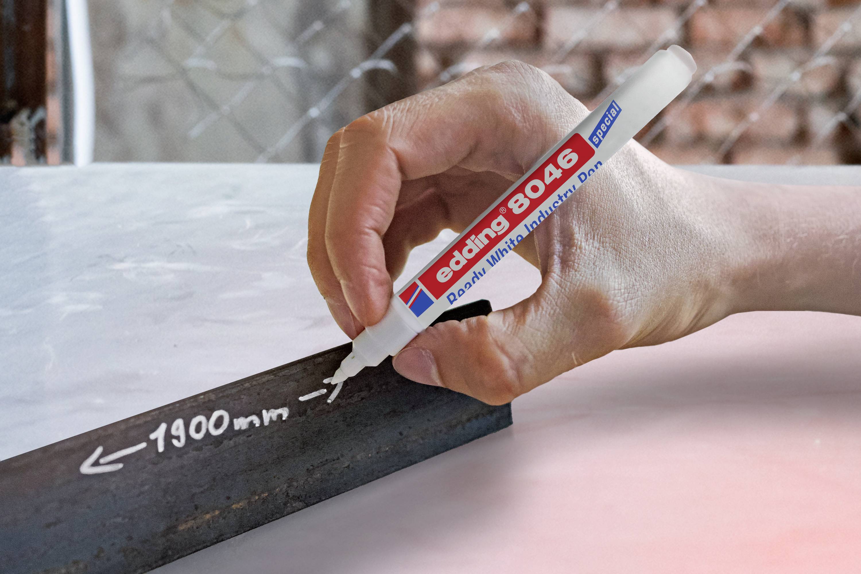 Eine Hand schreibt mit einem weißen Marker '1900 mm' auf ein Metallstück.