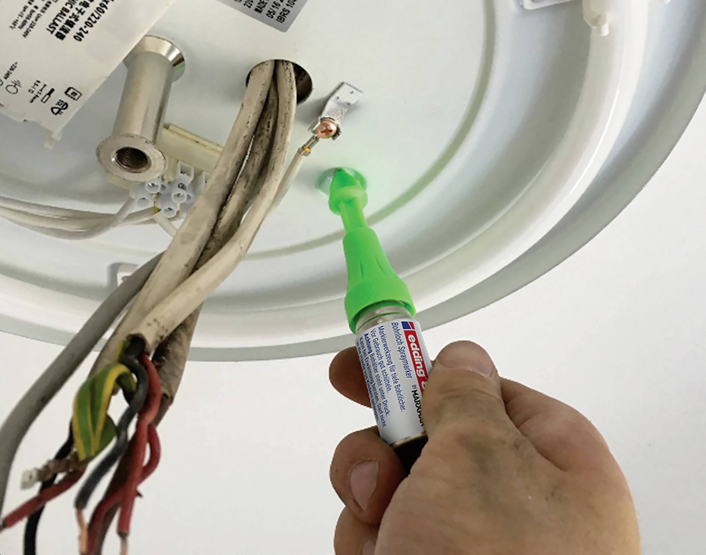 Hand hält einen Spannungsprüfer an einer Kabelverbindung an der Decke, um elektrische Spannung zu überprüfen. Ein grünes Licht leuchtet.
