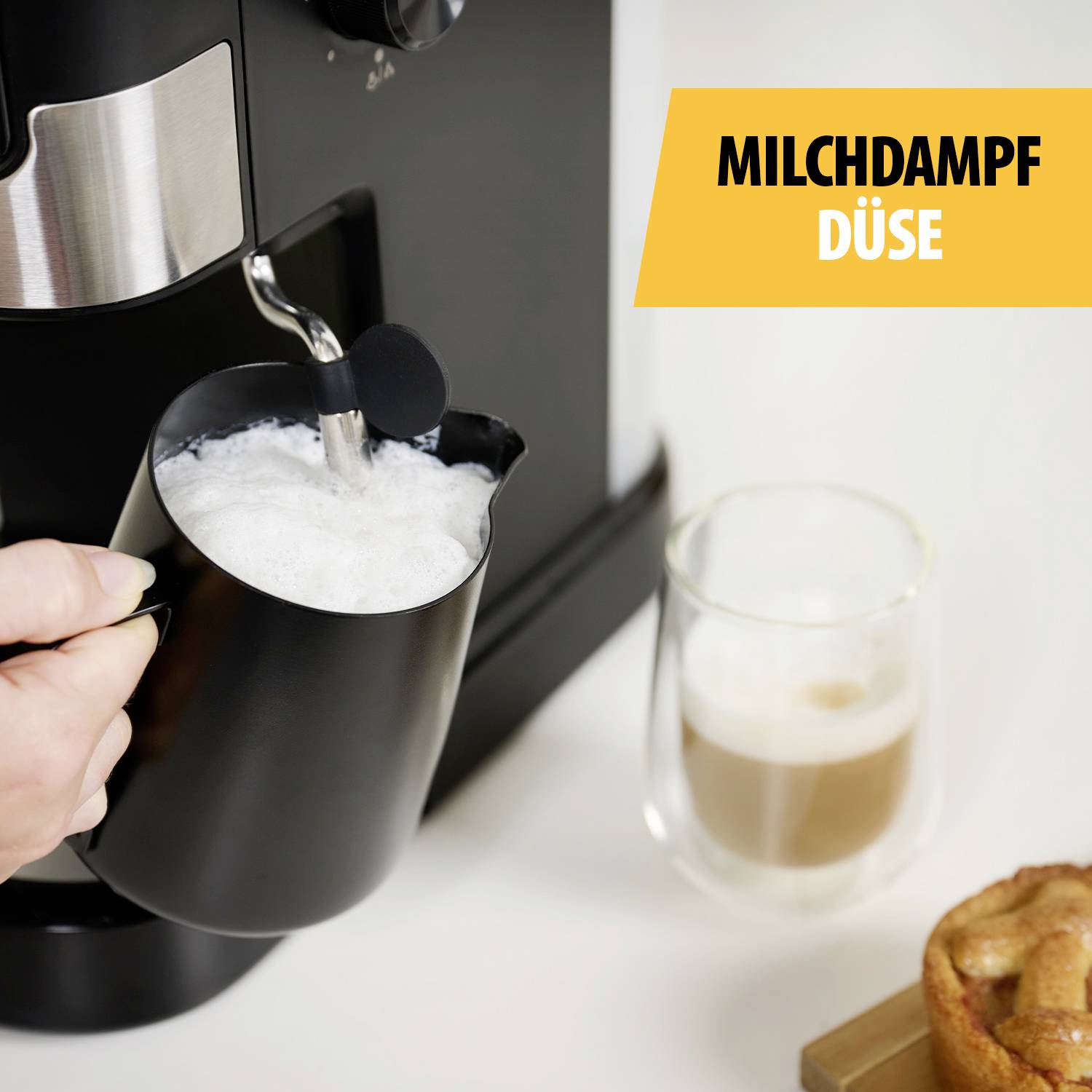 Eine Hand schäumt Milch in einem Krug mit einer Espressomaschine auf. Rechts oben ist ein gelbes Feld mit der Aufschrift 'Milchdampfdüse'.