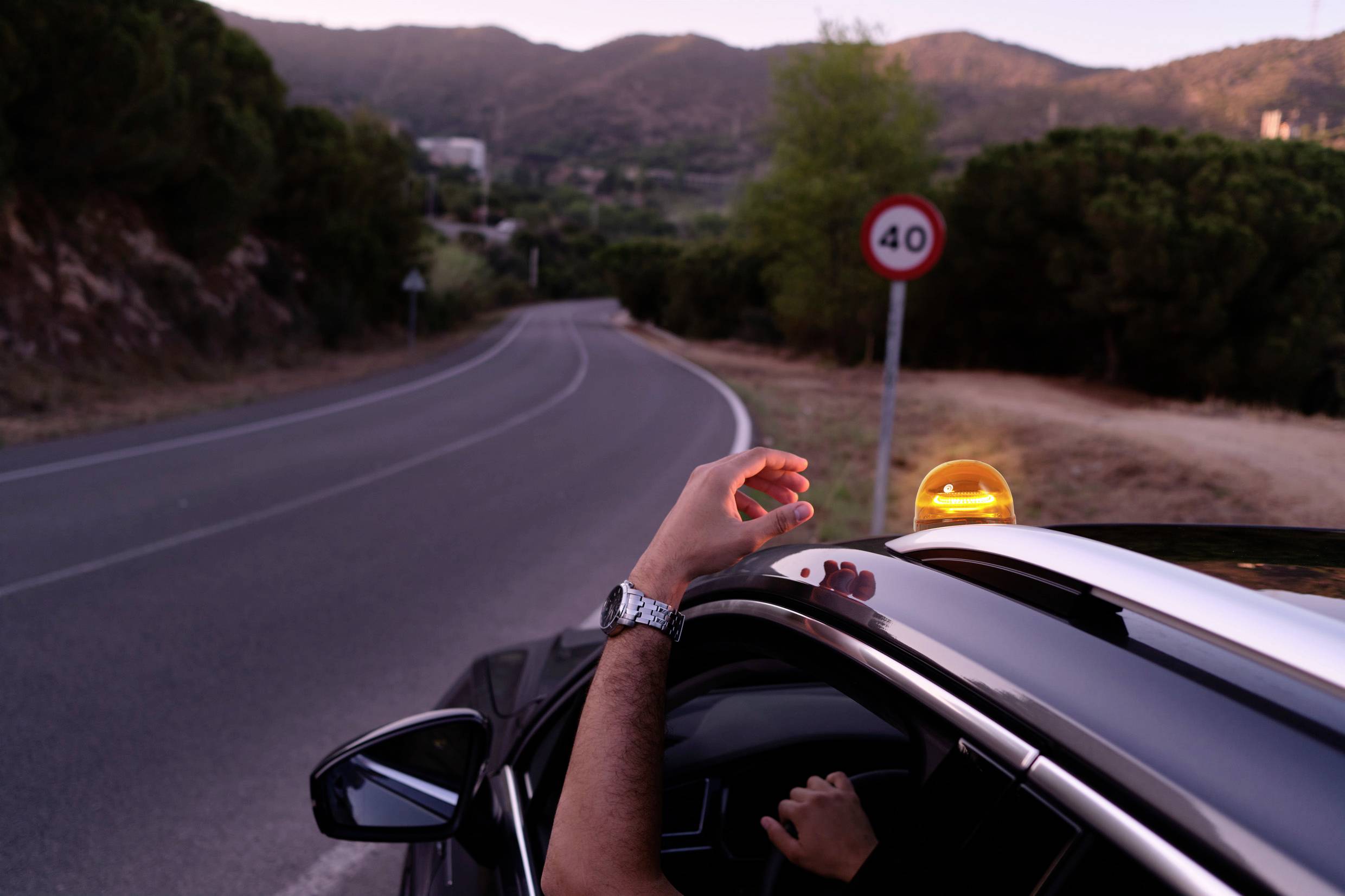 Ein Auto fährt auf einer kurvigen Landstraße in einer bergigen Gegend. Das Geschwindigkeitslimit beträgt 40 km/h.
