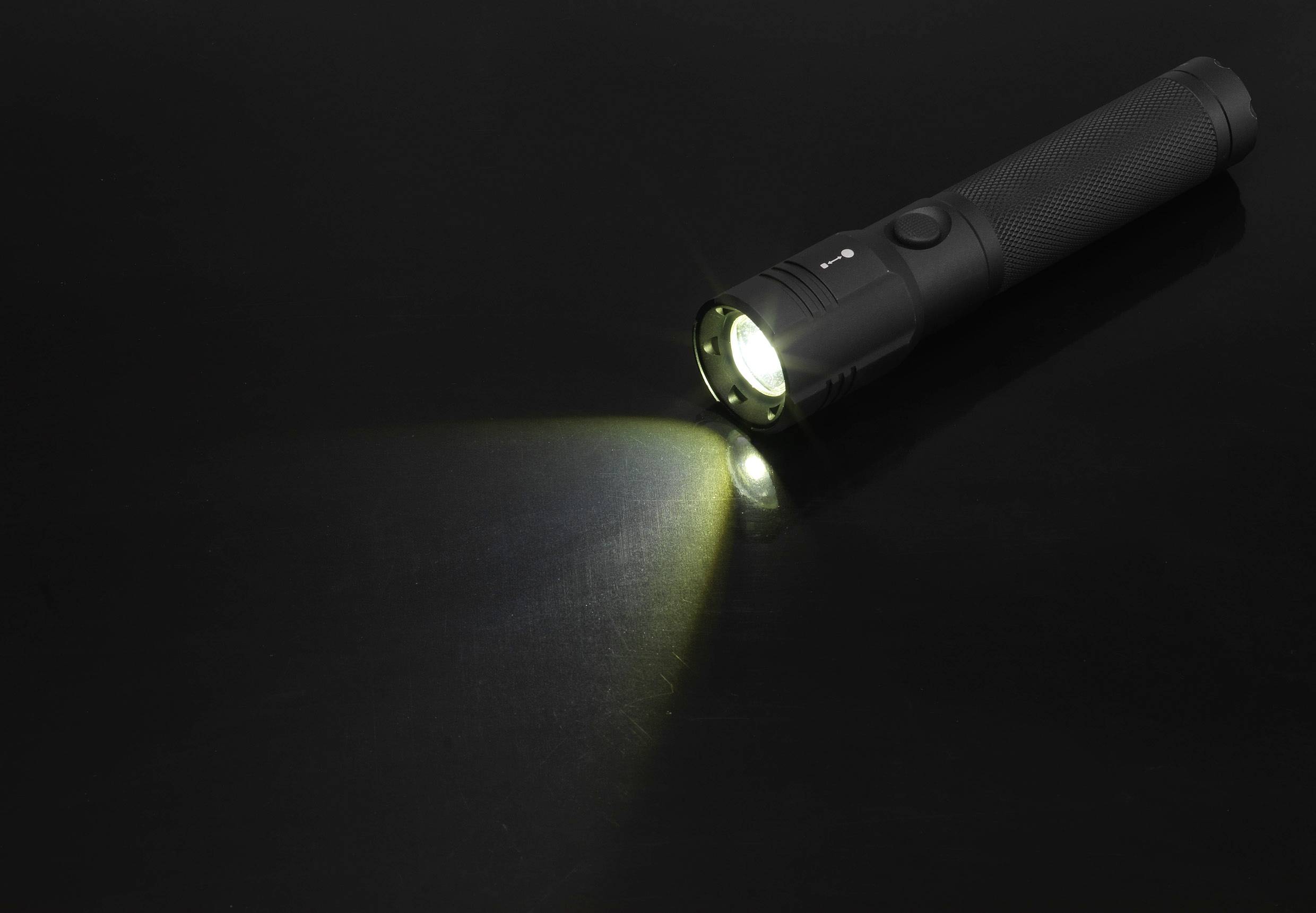 Schwarze Taschenlampe leuchtet auf schwarzem Hintergrund, Lichtstrahl nach links.