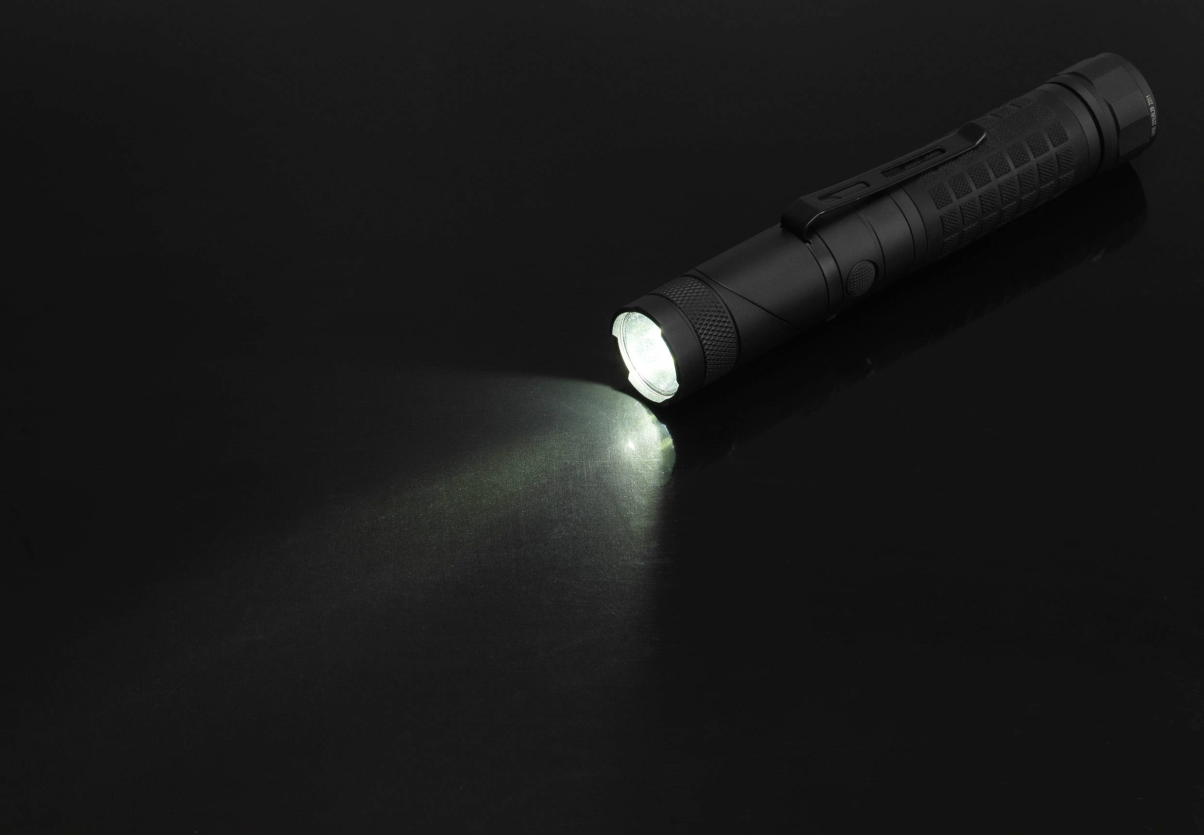 Schwarze Taschenlampe in dunkler Umgebung leuchtet helle Lichtkegel nach vorn.