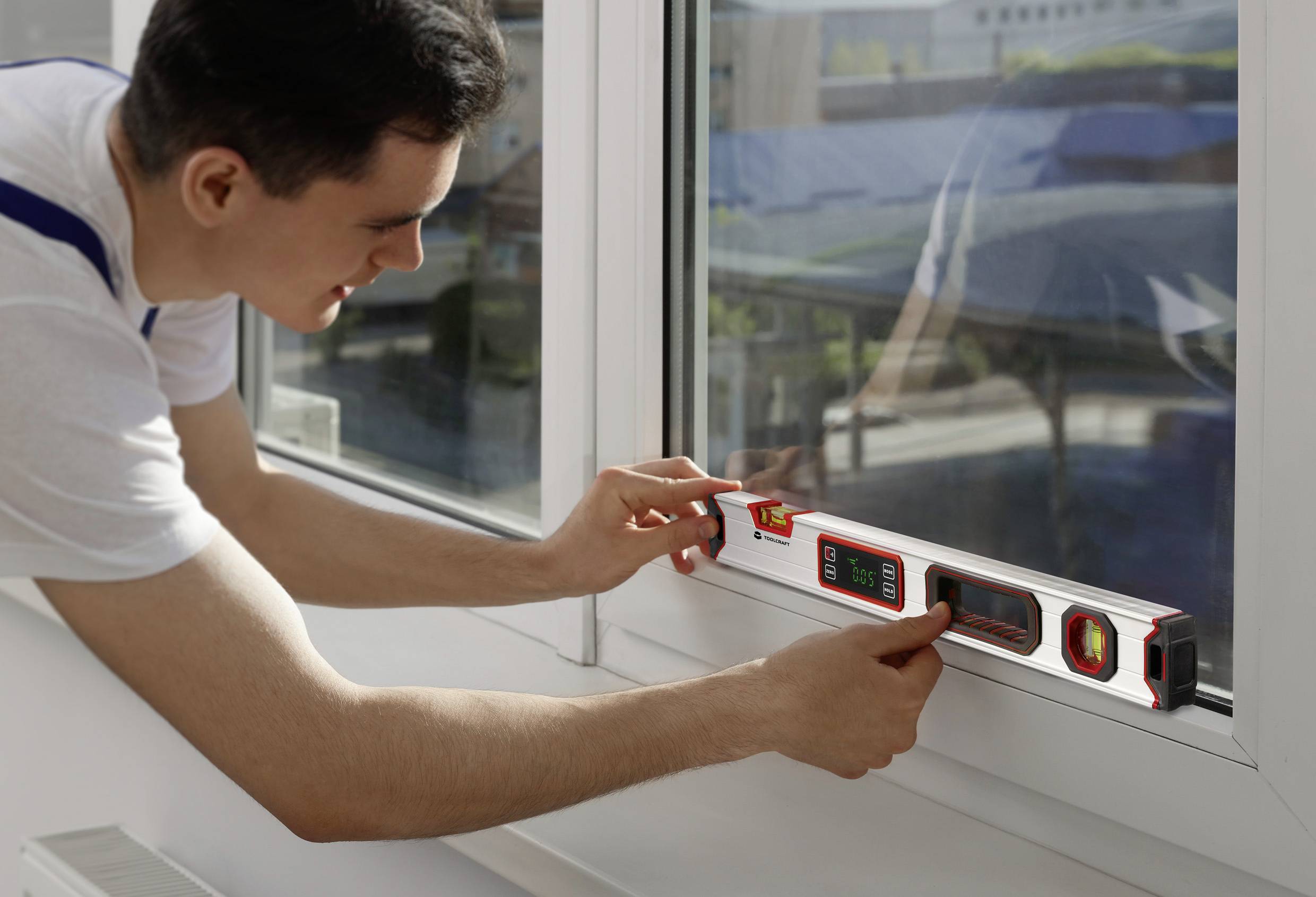 Ein Mann überprüft mit einer Wasserwaage die Ausrichtung eines Fensterrahmens. Er konzentriert sich auf die genaue Positionierung.