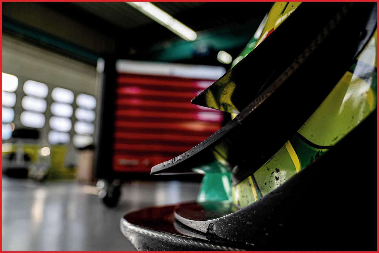 Nahaufnahme eines mehrfarbigen Objekts mit scharfen Kanten im Vordergrund; unscharfer Werkzeugschrank im Hintergrund einer Werkstatt.