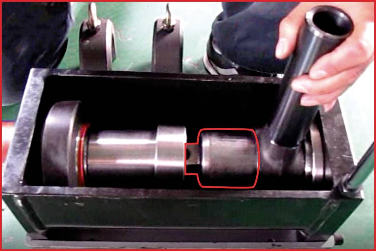 Eine Person bedient eine hydraulische Maschine mit einem Metallbauteil. Ein Bauteil im Inneren des Gehäuses ist rot markiert.