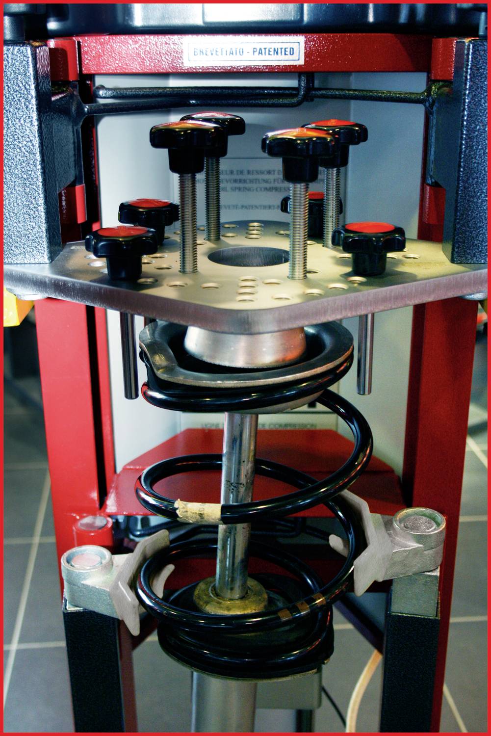 Maschine zur Federkompression in heller Umgebung. Metallkomponenten sichtbar, zeigt technische Details und Kompressionsmechanismus.