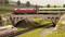 Eine Modelleisenbahnlandschaft zeigt eine rote und eine grüne Lok auf einer Brücke. Darunter fährt ein ICE-Zug auf einem anderen Gleis.