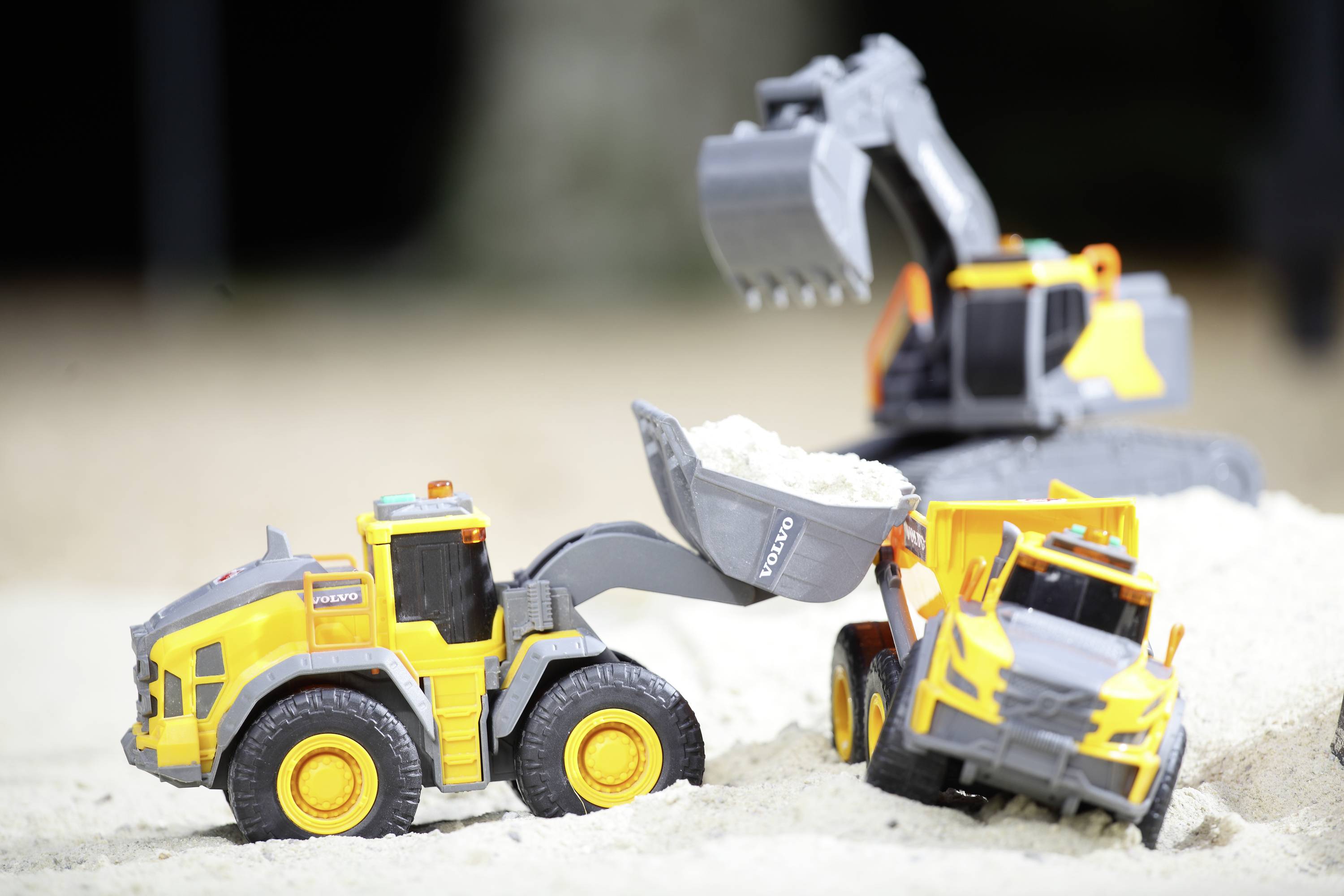 Spielzeugbagger und Lastwagen bewegen Sand in einem Kinder-Sandkasten.