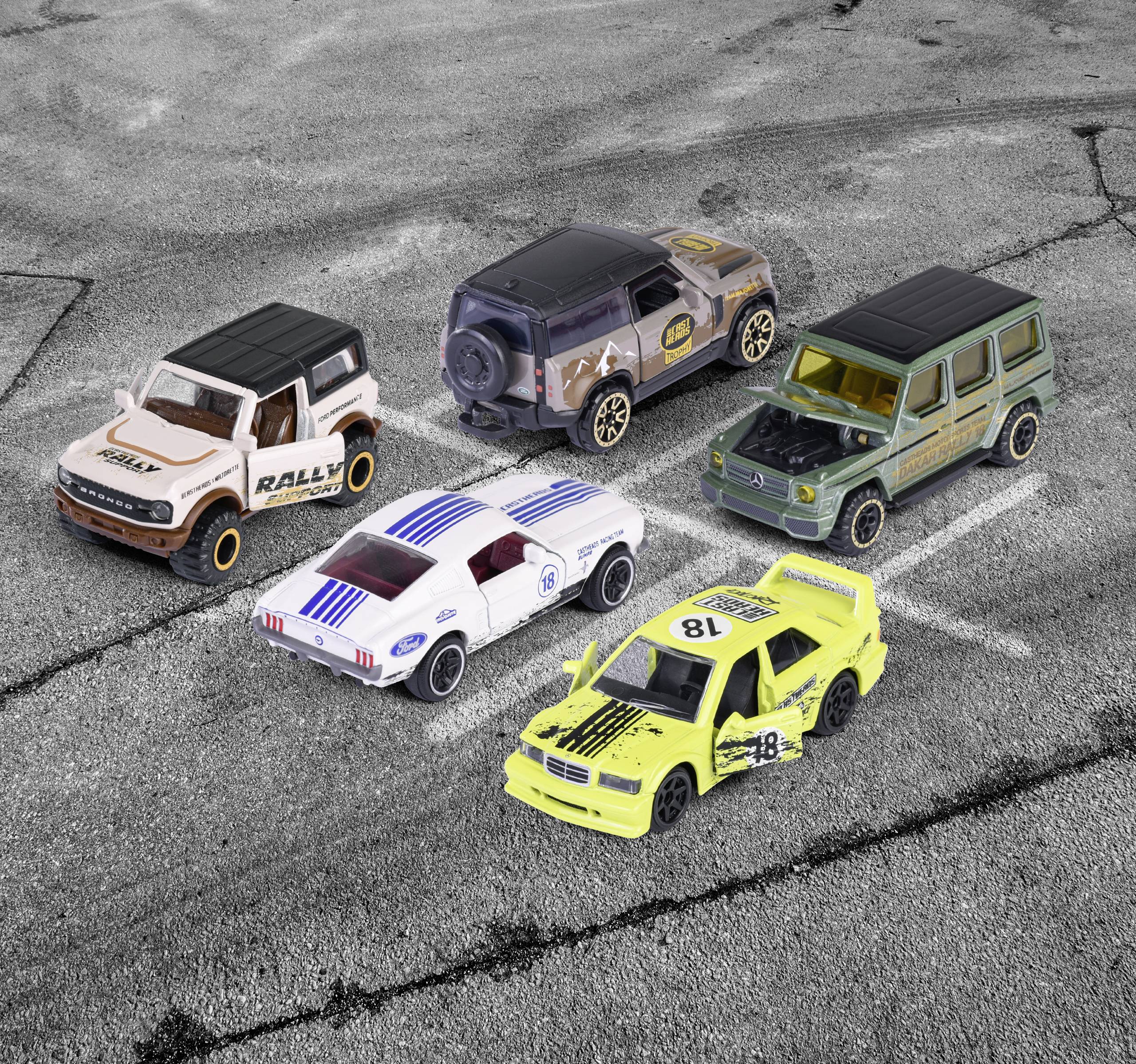 Fünf Spielzeugautos stehen auf einem grauen Asphalt. Zwei SUVs und drei Rennwagen in verschiedenen Farben und Designs.