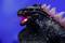 Ein schwarzer Dinosaurier mit leuchtenden Augen und rosa Stacheln brüllt vor einem blauen Hintergrund.