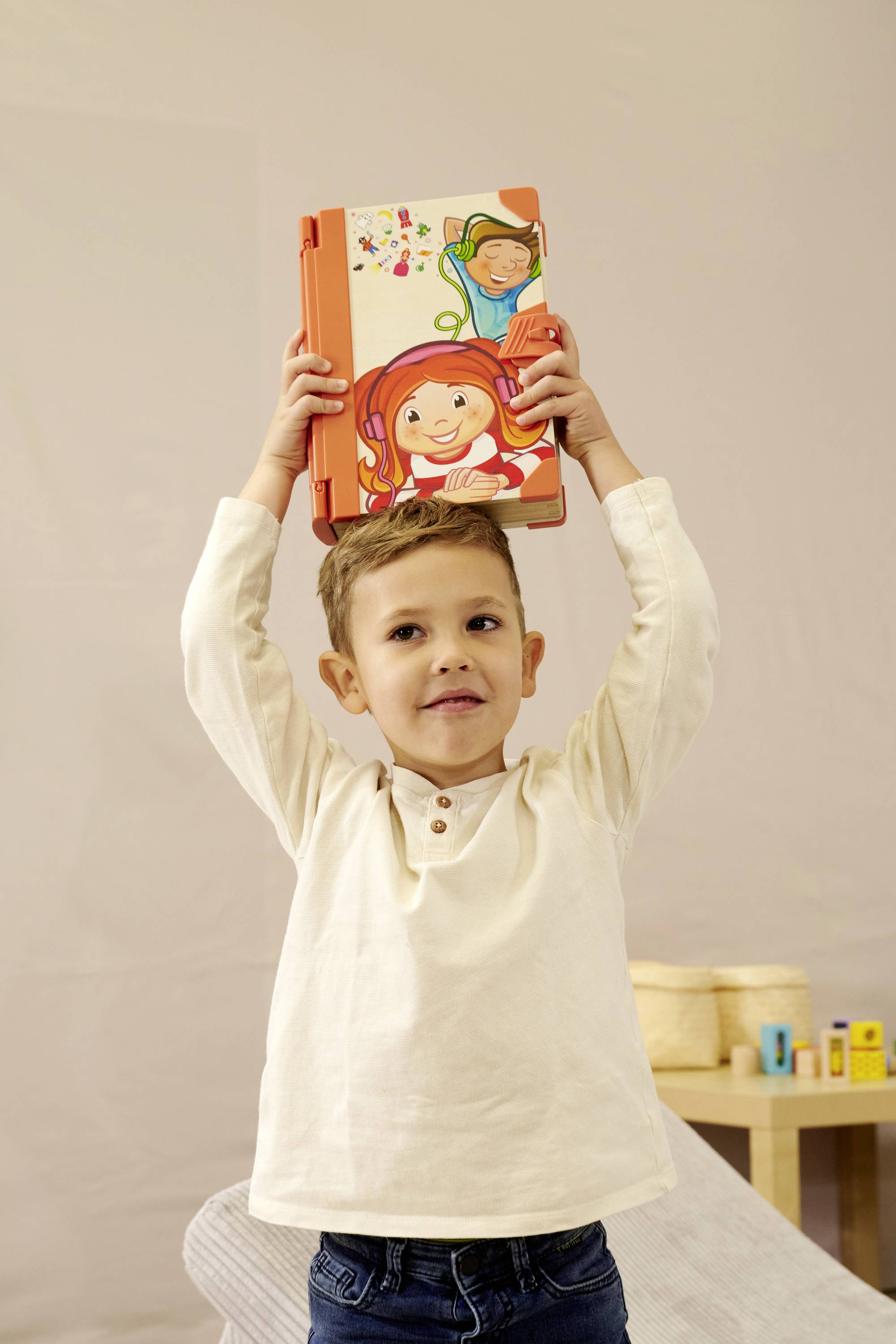 Ein Kind hält ein Bilderbuch hoch. Das Buch zeigt fröhliche Zeichnungen eines Kindes und Blumen. Im Hintergrund sind Möbel erkennbar.