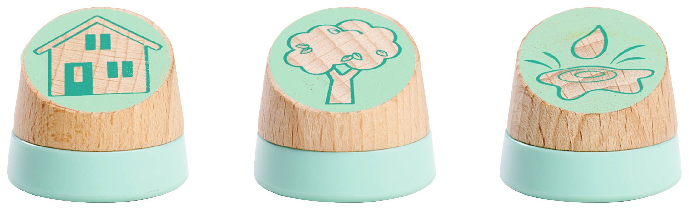 Drei Holzstempel mit runden Griffen. Die Stempel zeigen ein Haus, einen Baum und einen Wasserkräusel auf der grünen Oberfläche.