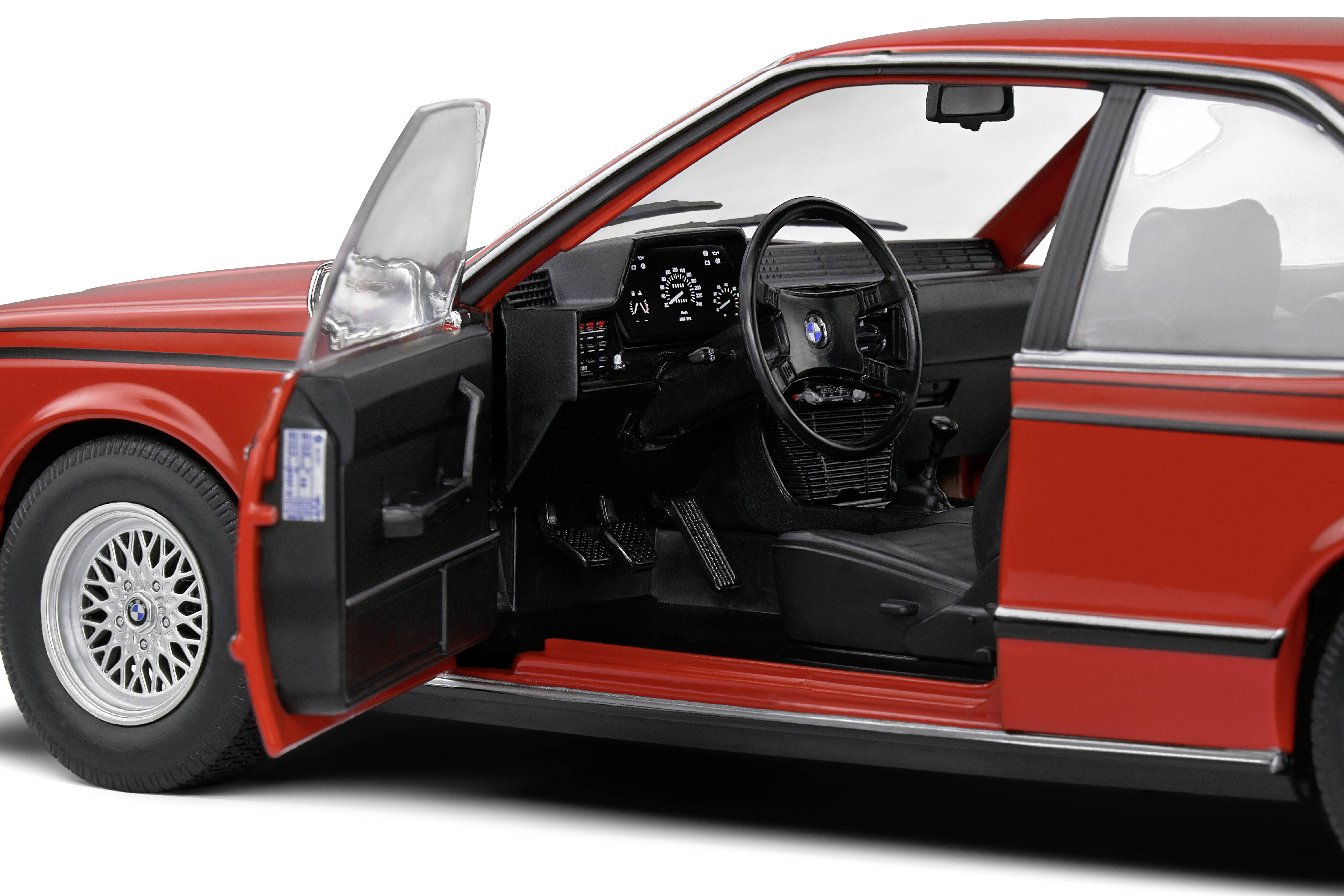 Ein rotes Modellauto mit geöffneter Fahrertür zeigt das Lenkrad und das Armaturenbrett detailliert. Fahrzeuginterieur sichtbar.