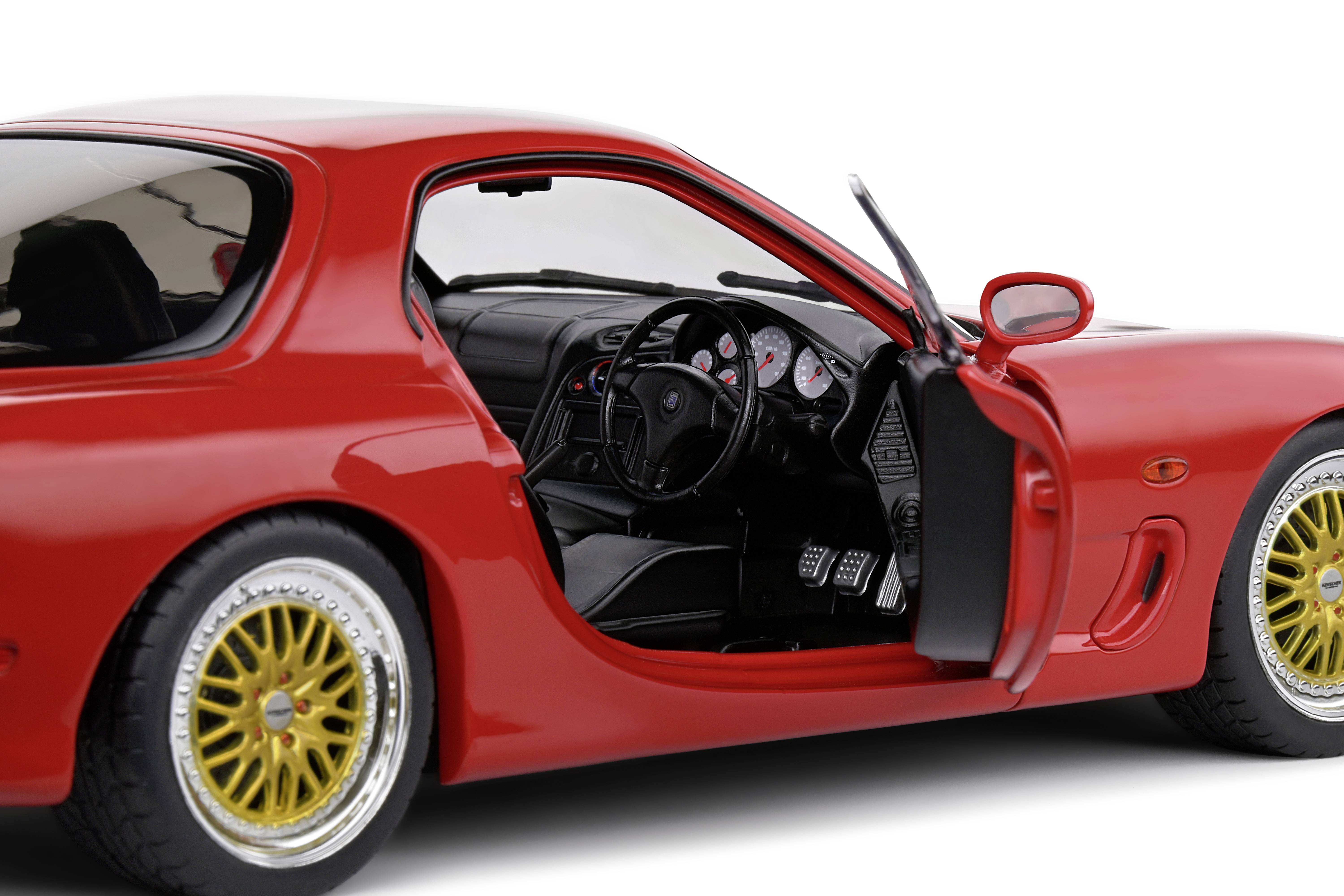 Ein rotes Sportauto-Modell mit geöffnetem Fahrerfenster. Sicht auf Armaturenbrett und Lenkrad, goldene Felgen. Rechte Seite gezeigt.