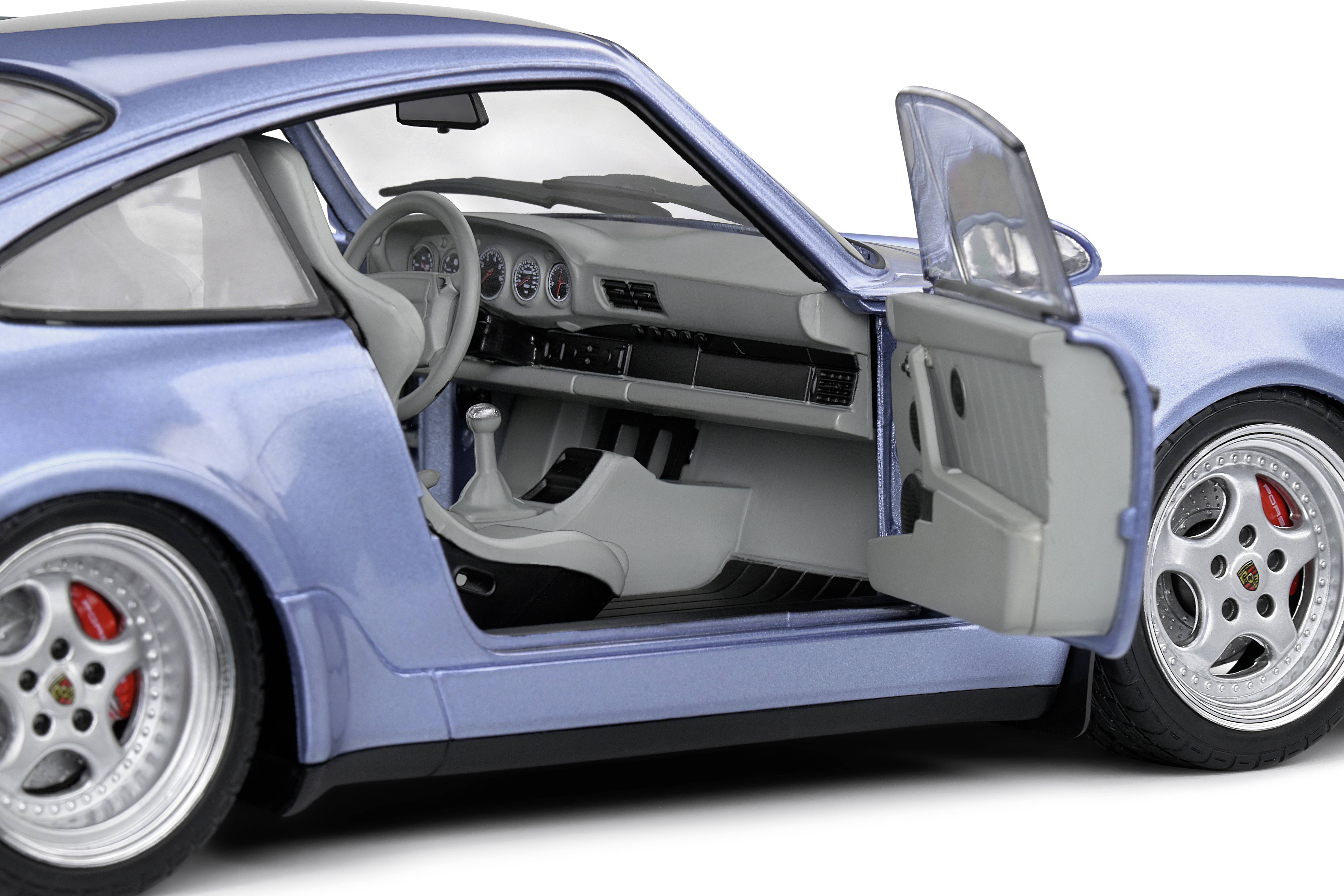 Silbernes Auto mit geöffneter Fahrertür; zeigt Innenraum mit Lenkrad, Schaltknüppel und Armaturenbrett-Details.