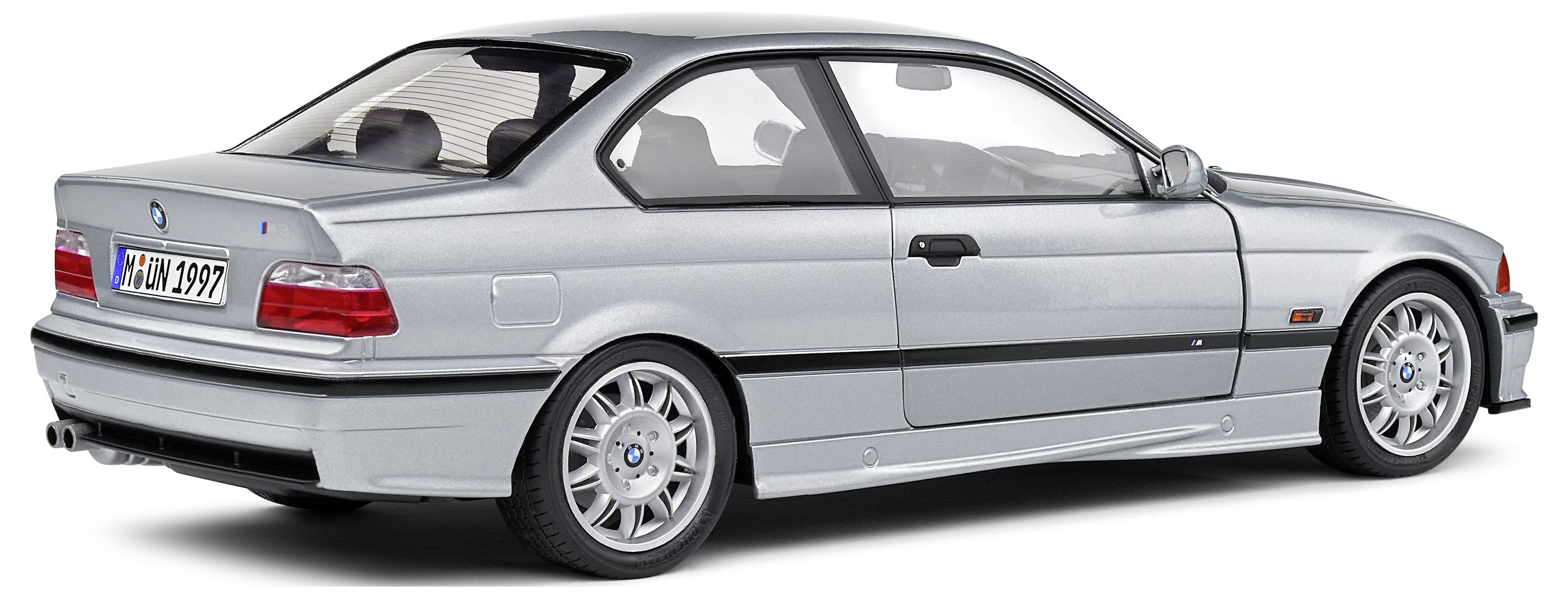 Silbernes Auto, seitliche Rückansicht, mit ausgeprägten Konturen und Leichtmetallfelgen; ruhige Szene ohne Bewegung.