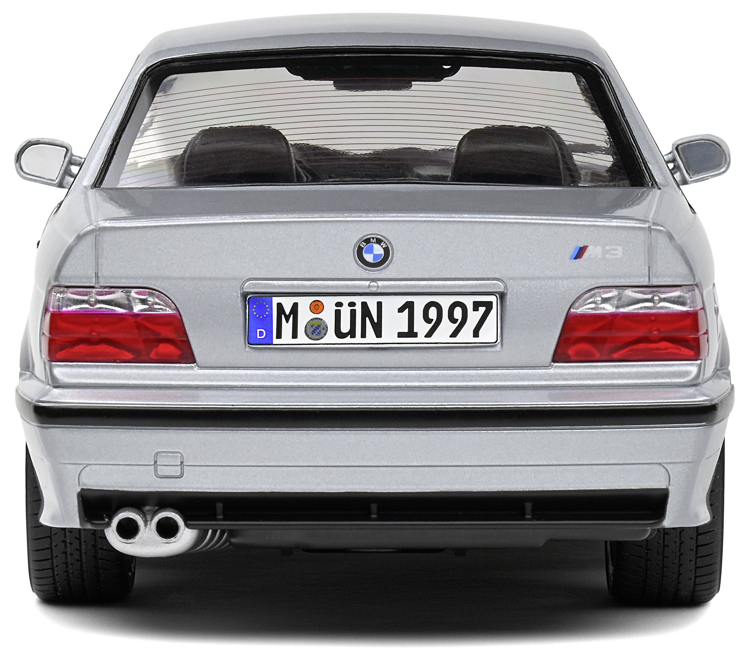 Ein silbernes Auto von hinten, mit deutschem Kennzeichen 'M ÜN 1997', sieht sportlich aus, mit Doppelauspuff.
