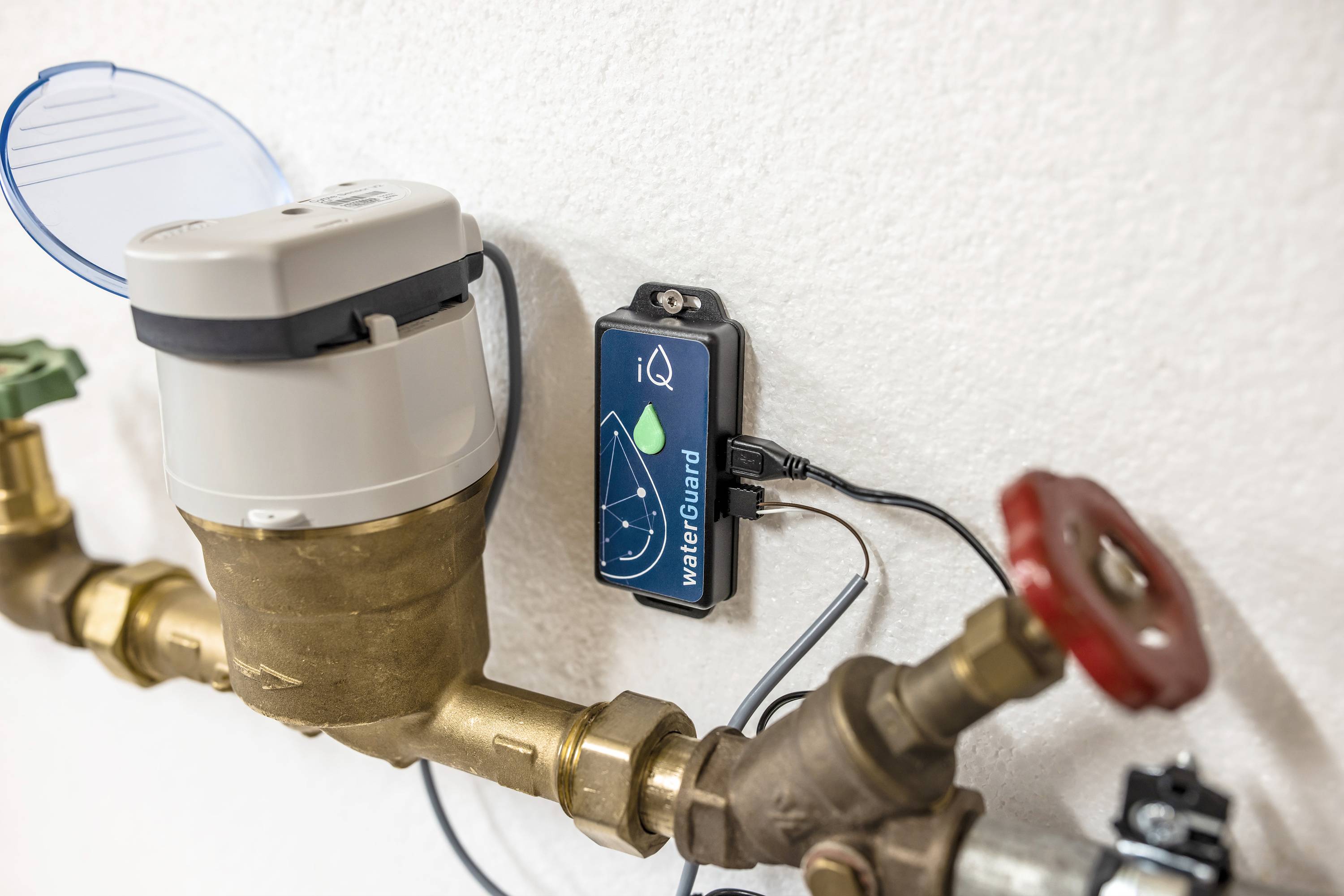 Ein Wasserzähler mit ablesbarem Display und elektronischem Steuergerät an einer Rohrleitung, an einer Wand montiert.