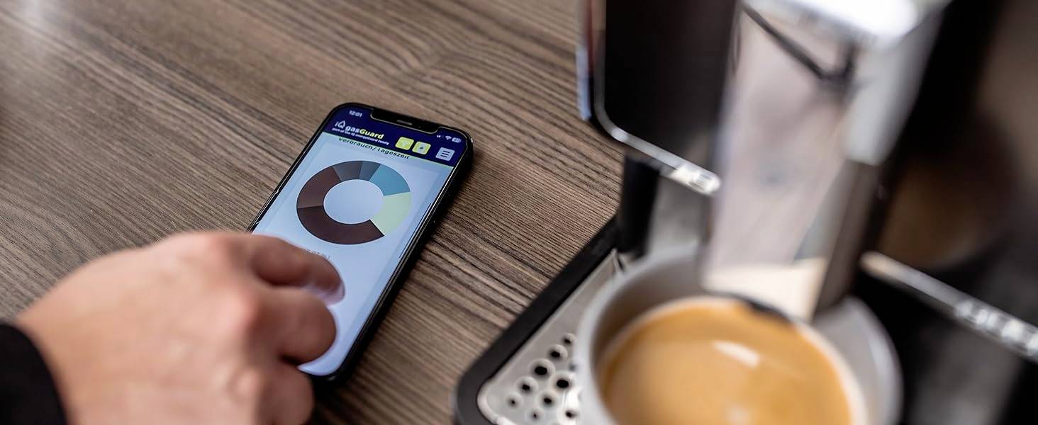 'Ein Smartphone zeigt ein Kreisdiagramm neben einer Kaffeemaschine, die Kaffee in eine Tasse gießt.'