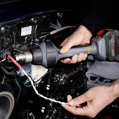 Eine Person verwendet eine Heißluftpistole an einem technischen Gerät. Die Szene zeigt eine präzise Arbeit mit Fokus auf Detailtreue.