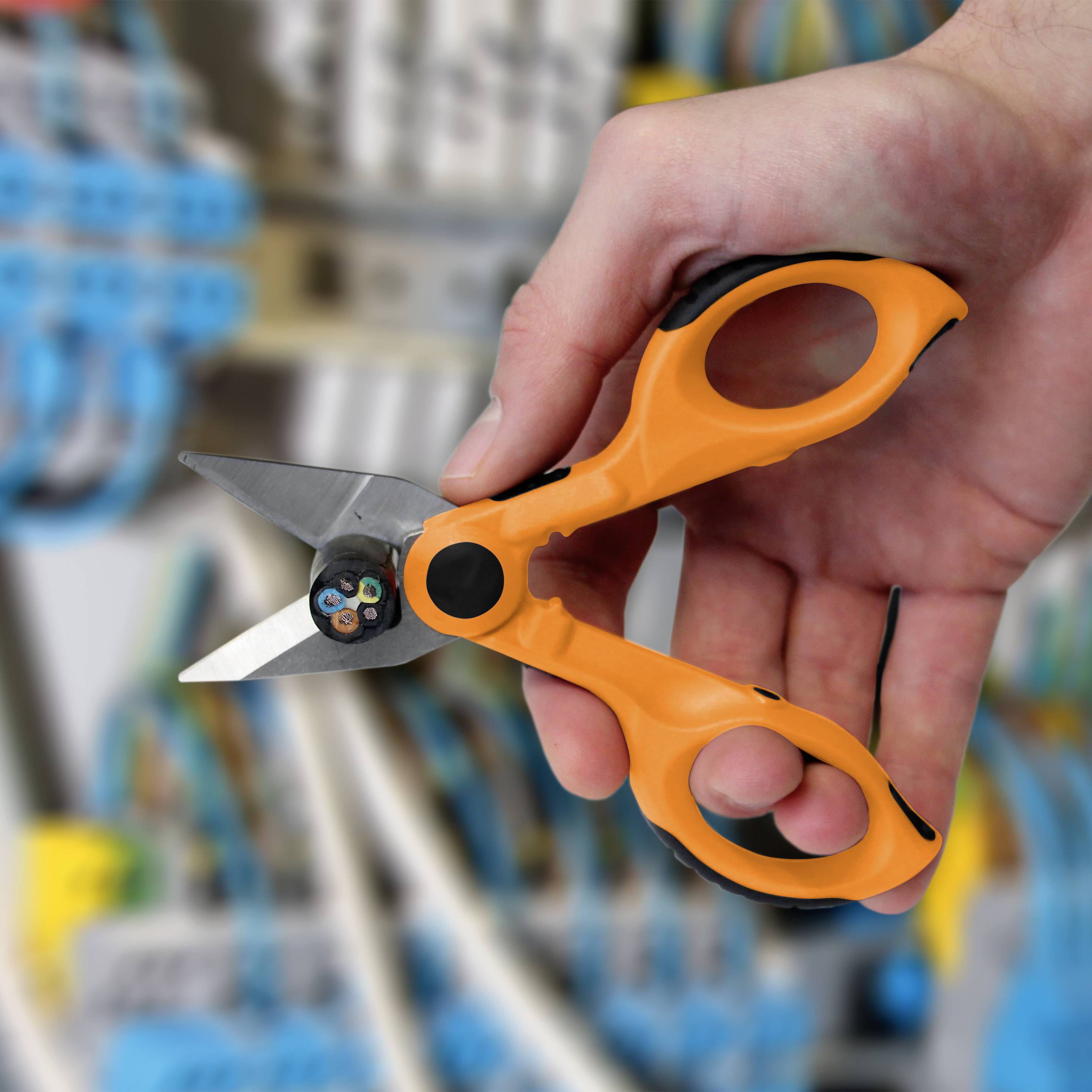 Hand hält eine Kabelschere, bereit, ein Kabel in einer elektrischen Schalttafel zu schneiden. Hintergrund zeigt verschwommene Kabel.