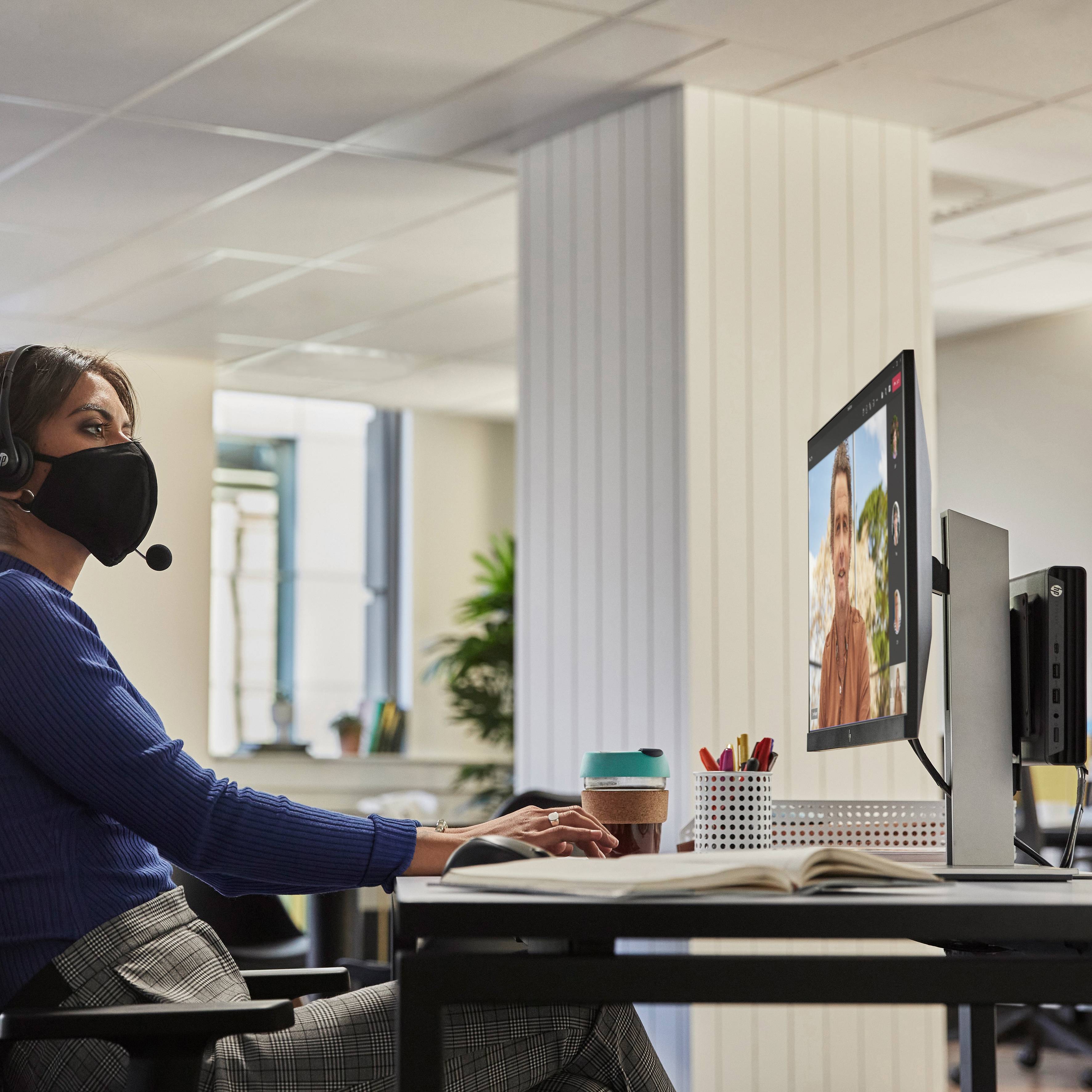 Eine Person mit Headset sitzt am Schreibtisch und nimmt per Videokonferenz an einem virtuellen Treffen teil.