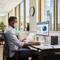 Eine Person mit Maske arbeitet an einem Computer im Büro. Auf dem Bildschirm: ein Kreisdiagramm und Balkendiagramme.