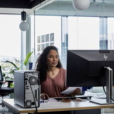 Eine Person sitzt an einem Schreibtisch in einem modernen Büro und arbeitet mit einem Computer, umgeben von Bürogeräten und Pflanzen.