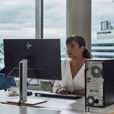 Frau sitzt im Büro, arbeitet konzentriert am Computer. Ein moderner Arbeitsplatz mit großem Monitor und Desktop-PC. Fensterausblick auf Stadt.