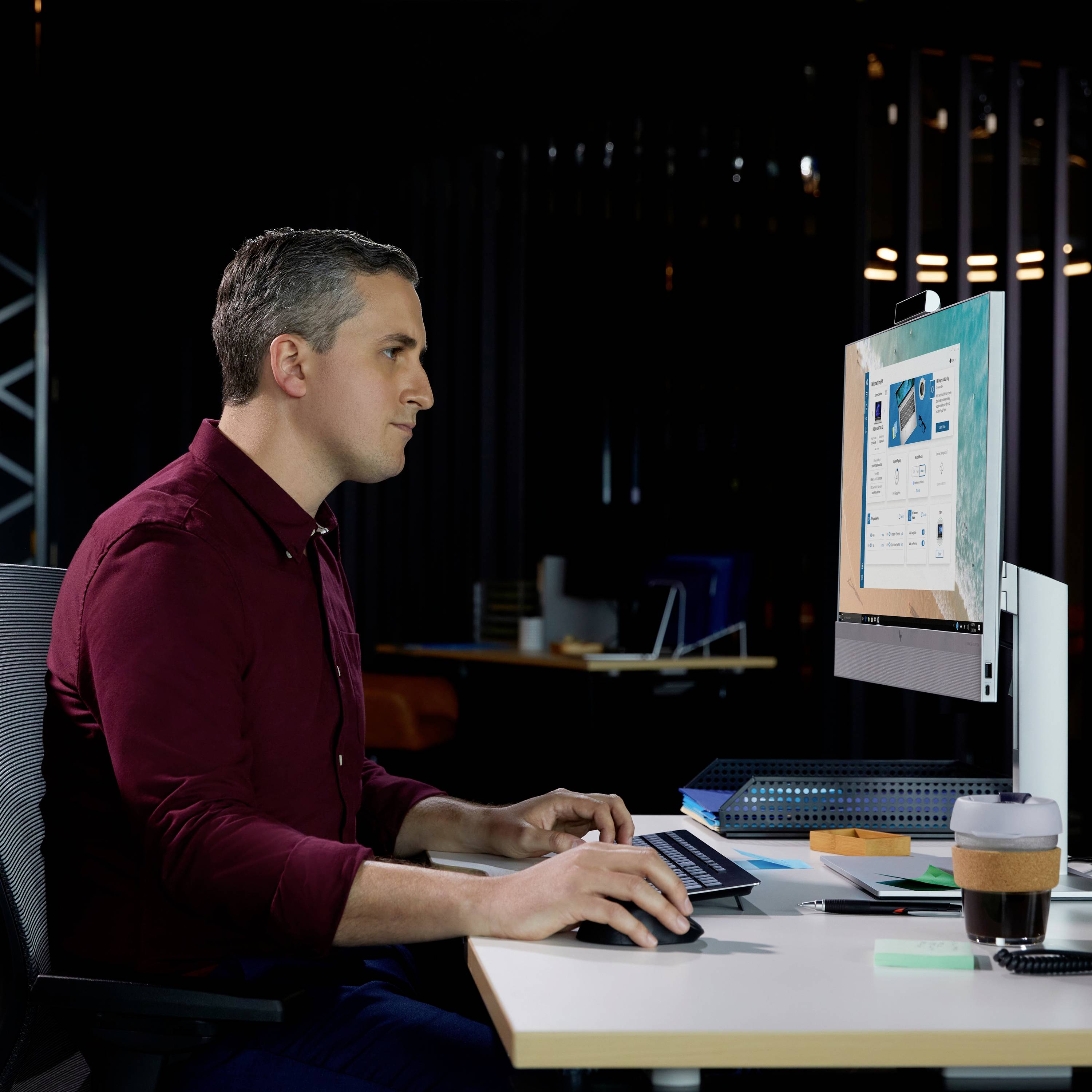 Eine Person arbeitet an einem Computer in einem modernen Büro, konzentriert auf die Aufgaben am Bildschirm. Bürobeleuchtung im Hintergrund.