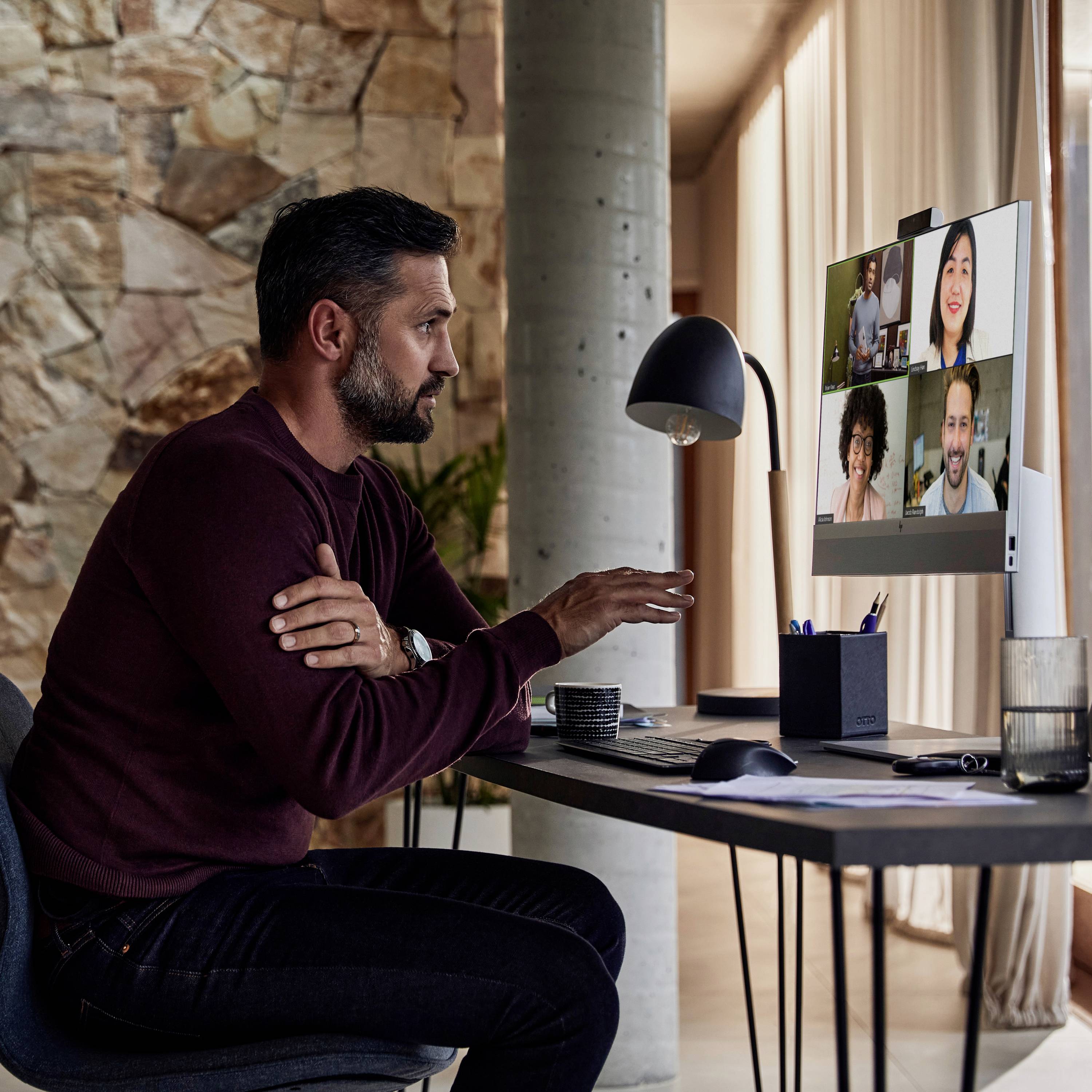 Ein Mann sitzt an einem Tisch und nimmt an einer Videokonferenz mit mehreren Teilnehmern auf einem Computerbildschirm teil.