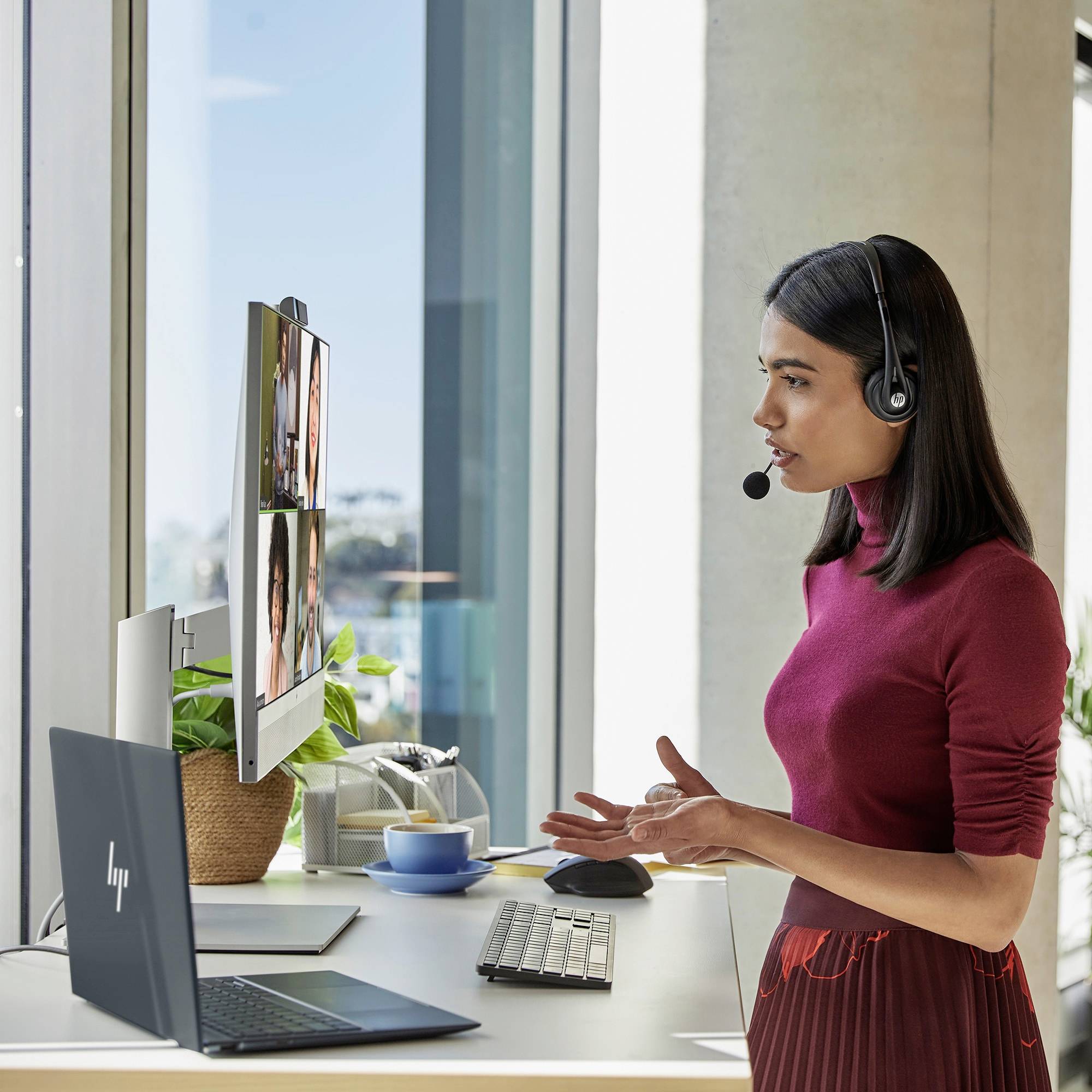 Frau mit Headset steht an einem Schreibtisch, arbeitet am Computer und führt ein Videotelefonat.