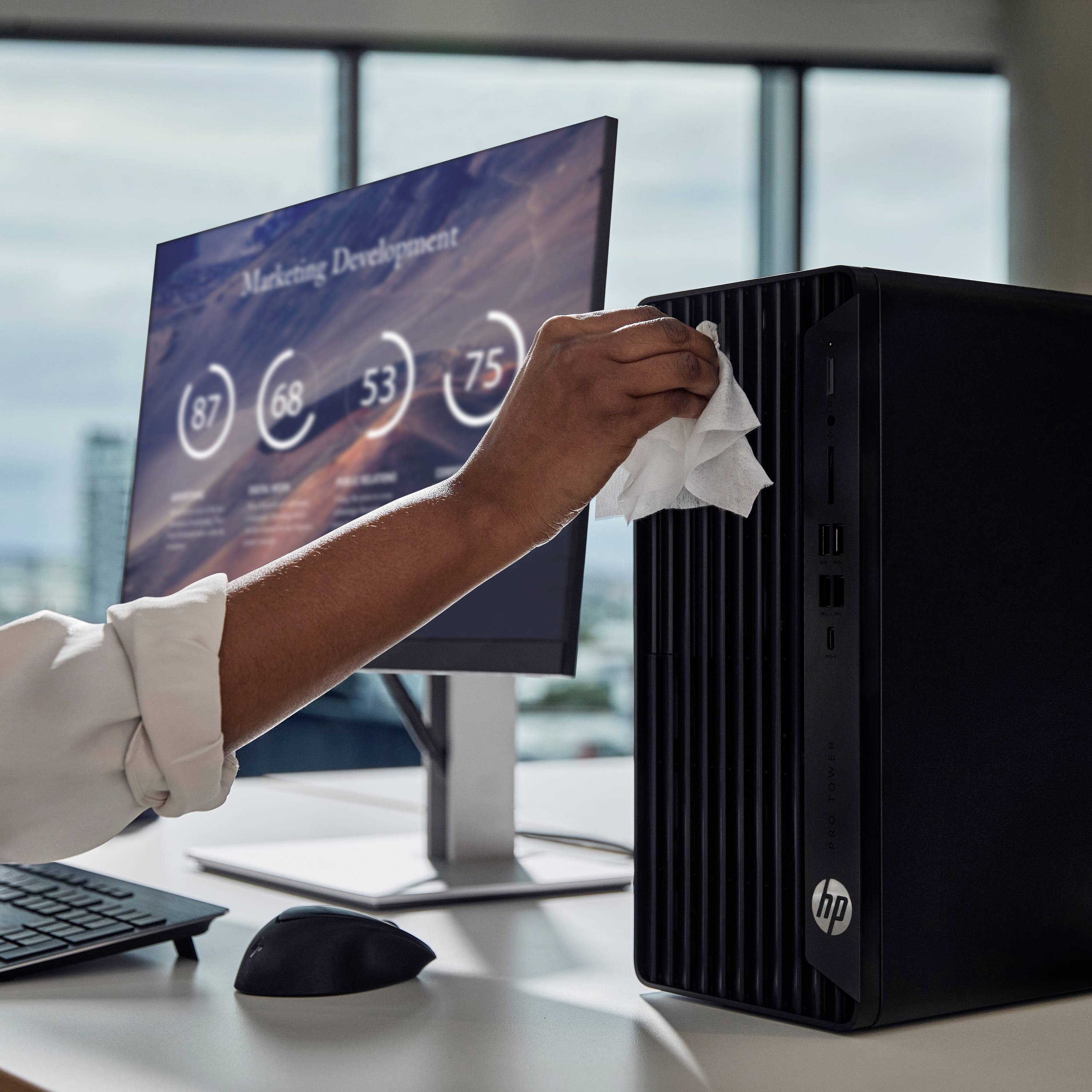 Eine Person reinigt einen Desktop-Computer in einem modernen Büro. Auf dem Monitor sind unscharfe Grafiken und Zahlen zu sehen.