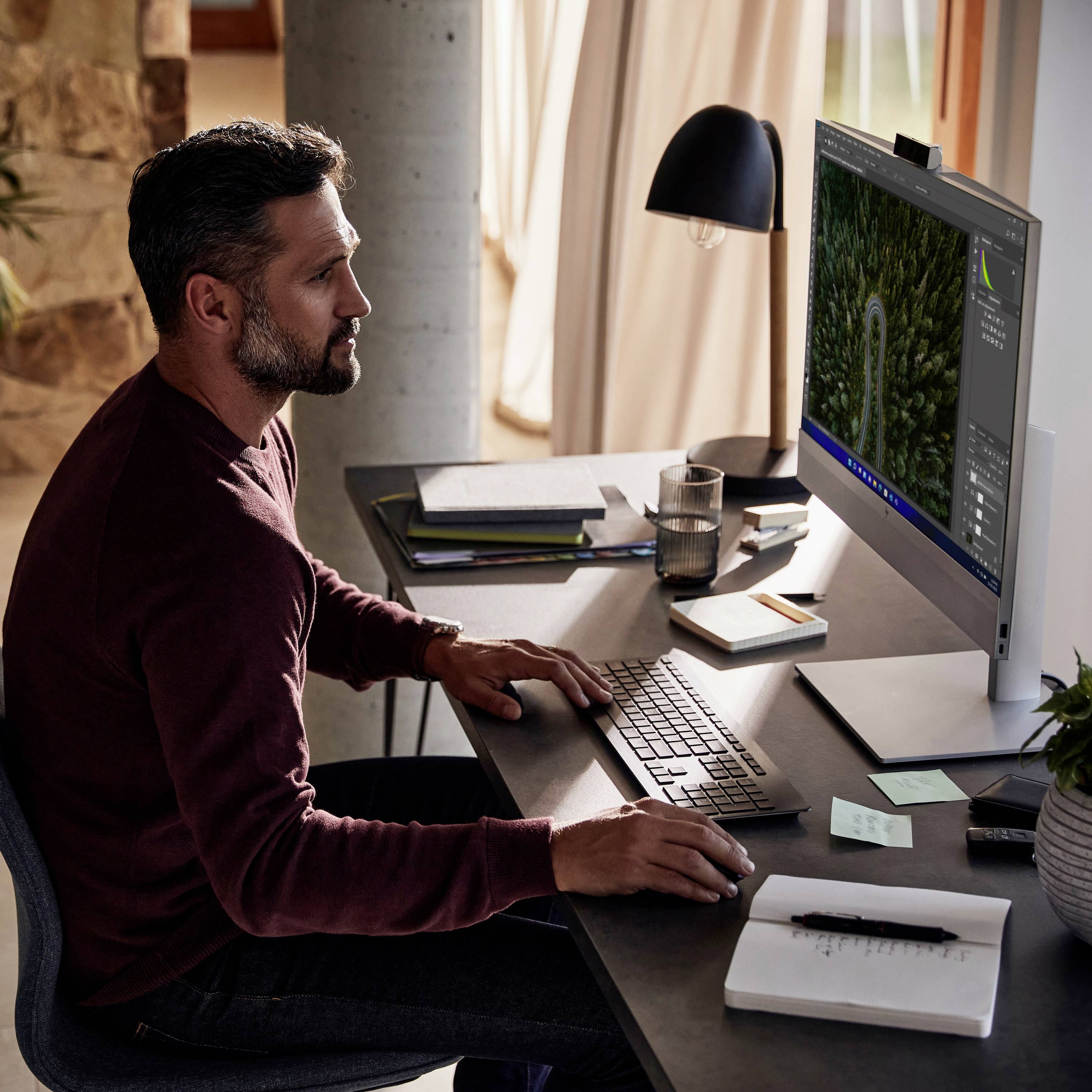 Ein Mann sitzt vor einem Computer und bearbeitet ein Bild vom Wald auf dem Bildschirm. Der Raum ist gemütlich und gut beleuchtet.
