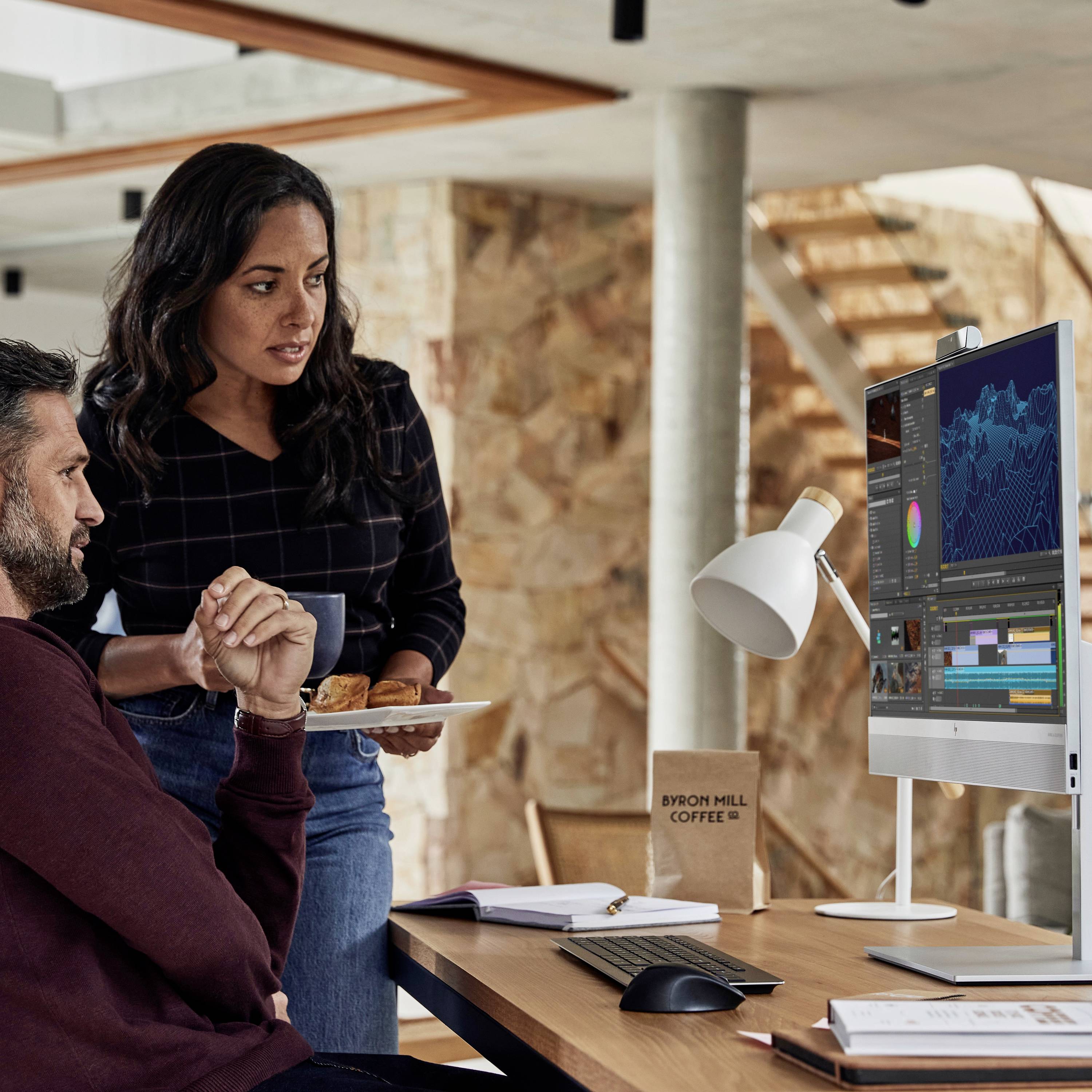 Eine Frau und ein Mann arbeiten an einem Computer in einem modernen Büro. Sie zeigt auf den Bildschirm, während er sich Notizen macht.