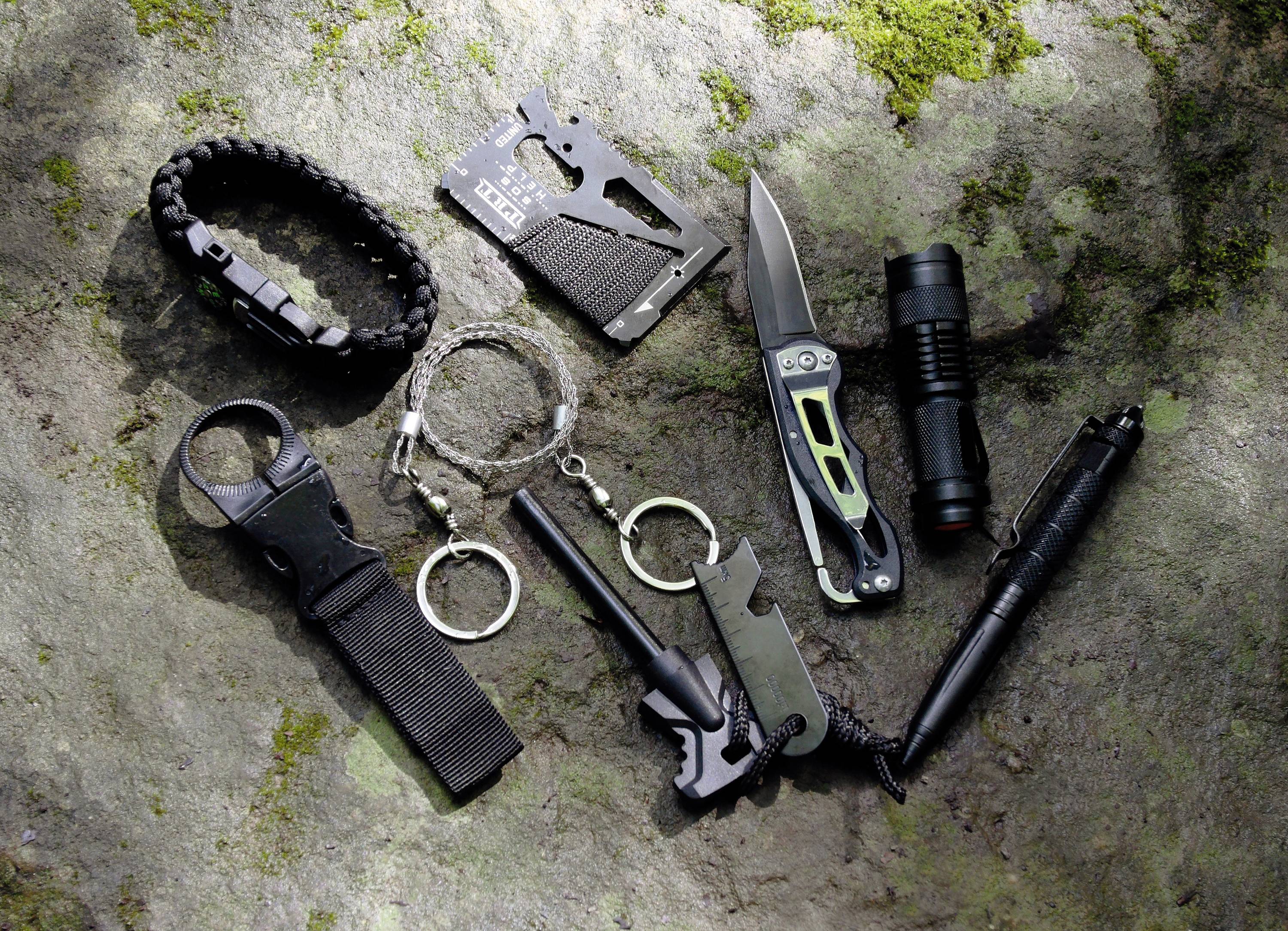 Überlebensausrüstung auf einem Stein: Armband, Mehrzweckwerkzeug, Messer, Taschenlampe, Streichstahl, Schlüsselanhänger-Werkzeug.