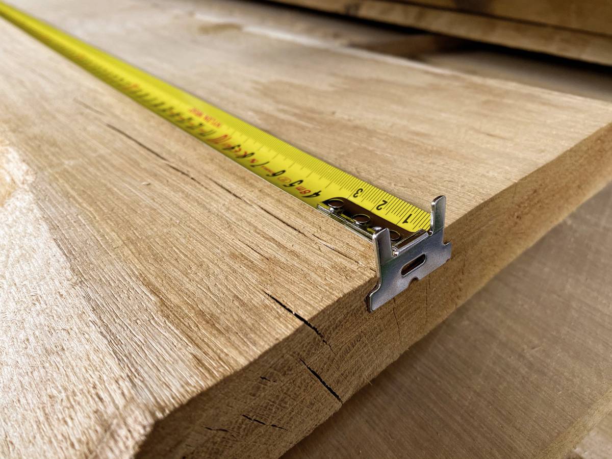 Nahaufnahme eines Holzbretts mit einem gelben Maßband darauf. Das Maßband zeigt eine genaue Länge an und liegt diagonal auf dem Brett.